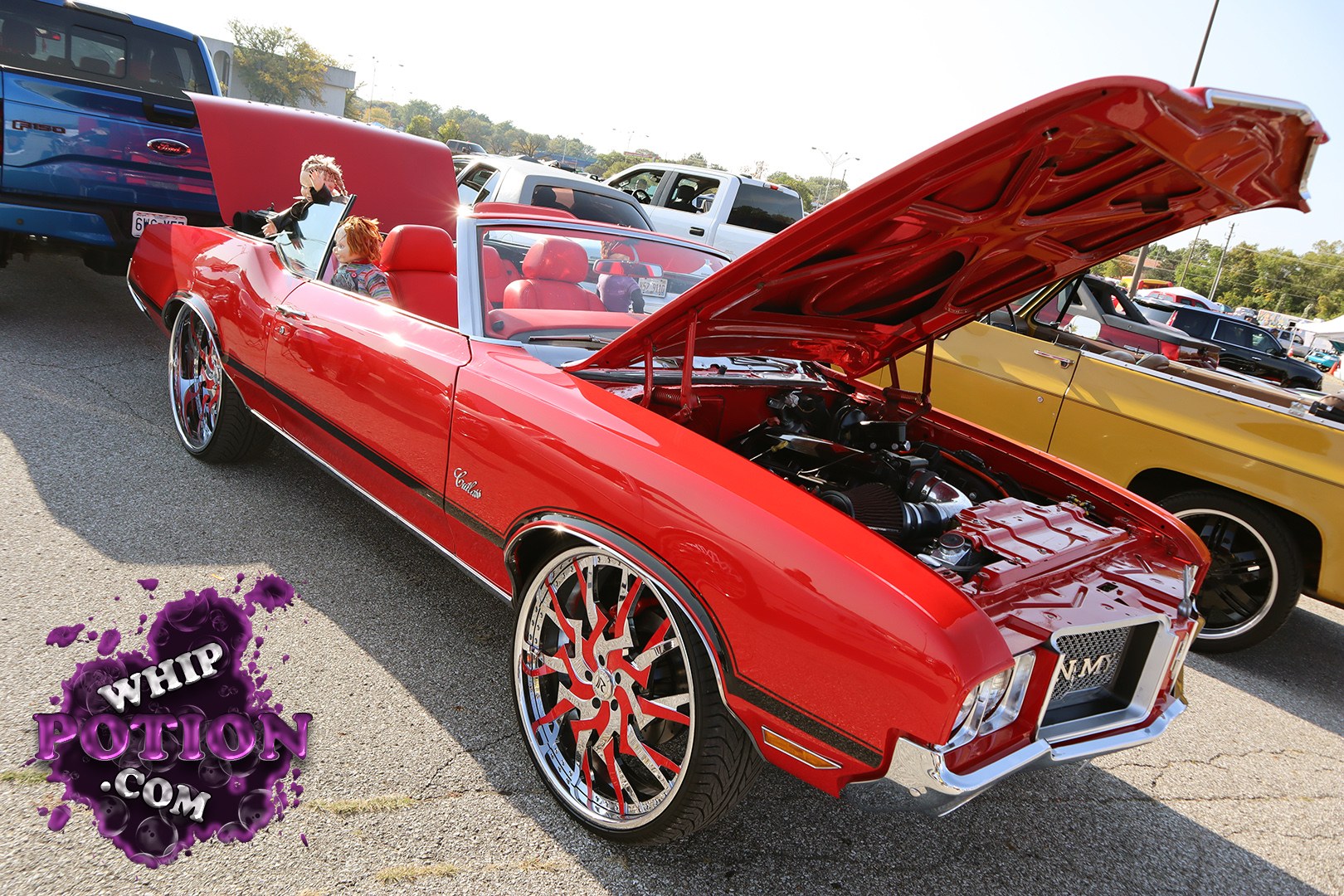 A red Cadillac Eldorado convertible gets the full custom treatment here, with the hood popped to show off a dressed-up bay and the top down over matching red interior. The big billet-style wheels, thin side trim, and that long, low profile give it a sharp boulevard-cruiser look without going over the top.