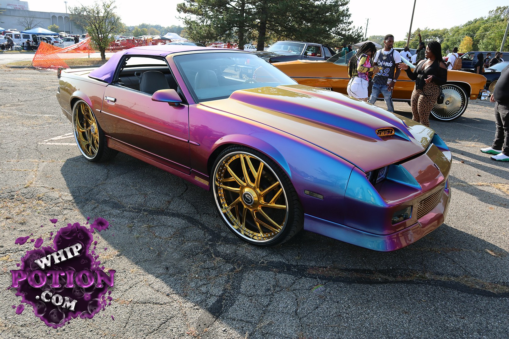 This Nissan 240SX gets a full custom treatment, with a wild purple-to-gold fade, a smooth body kit, and a functional-looking hood scoop marked “SWIFT.” The big gold stepped-lip wheels and low, clean stance give it a sharp street-ready look, while the purple soft top ties the whole build together with plenty of show-car attitude.