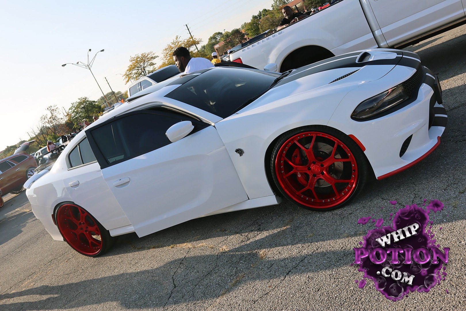 A white Dodge Charger with a black roof and hood gives off a clean, aggressive look, set off by deep-dish red wheels and a seriously low stance. The blacked-out grille and sharp front end keep it menacing, while the tinted glass and subtle side badging make the whole build feel dialed in without going overboard.