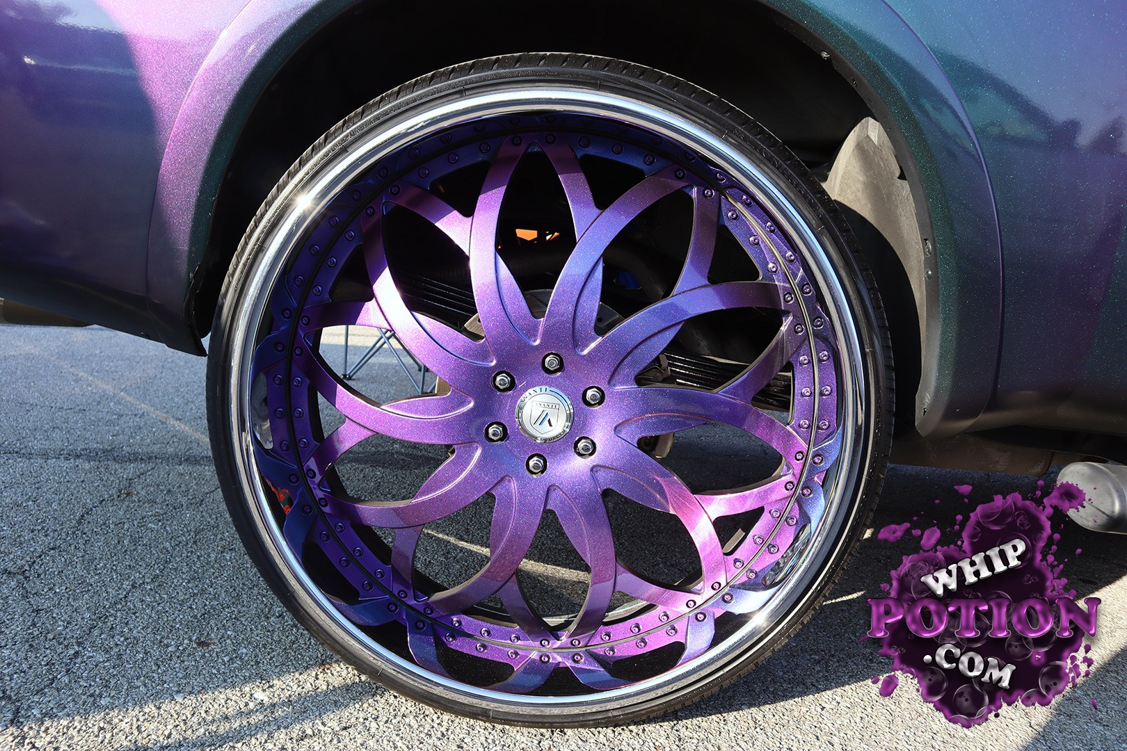 This custom ride leans hard on a wild purple-to-teal candy finish and an oversized billet wheel with a deep lip and sculpted multi-spoke face. The stretched tire, tucked fitment, and clean bodywork give it a serious show-car presence, and the color-matched details really set off the whole build.