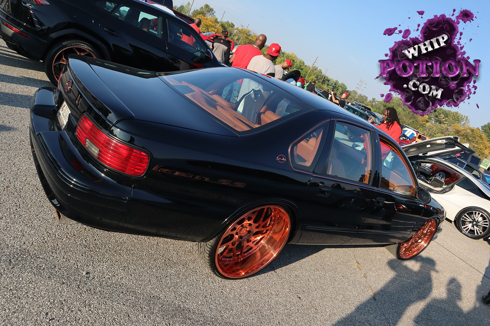 A black Chevrolet Impala SS sits low on copper oversized wheels, its dark paint and tan leather interior giving it a clean, custom look. The rear spoiler, smoked taillights, and subtle badging keep it unmistakably 90s GM, while the big-diameter setup gives the sedan a bold boulevard stance without losing its smooth cruiser vibe.