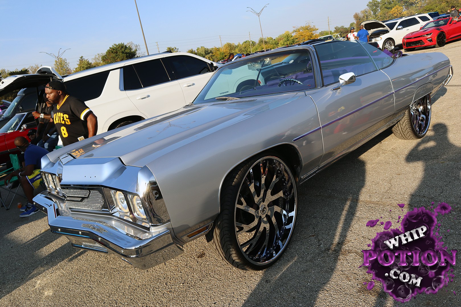 This classic Chevy Impala convertible brings full-size swagger with a smooth silver finish, chrome nose, and deep-dish black-and-machined wheels tucked under a clean, low stance. The purple accents inside and along the body give it a subtle custom touch without overdoing it, and the long, unmistakable lines make it pure boulevard material.