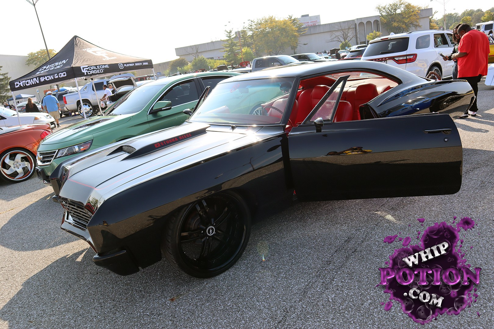 A slick black custom coupe with a long hood, shaved clean bodywork, and a vivid red interior that really pops against the paint. The hood scoop and bold stance give it a serious street presence, while the oversized black wheels and matching trim keep the whole build looking sharp and deliberate.