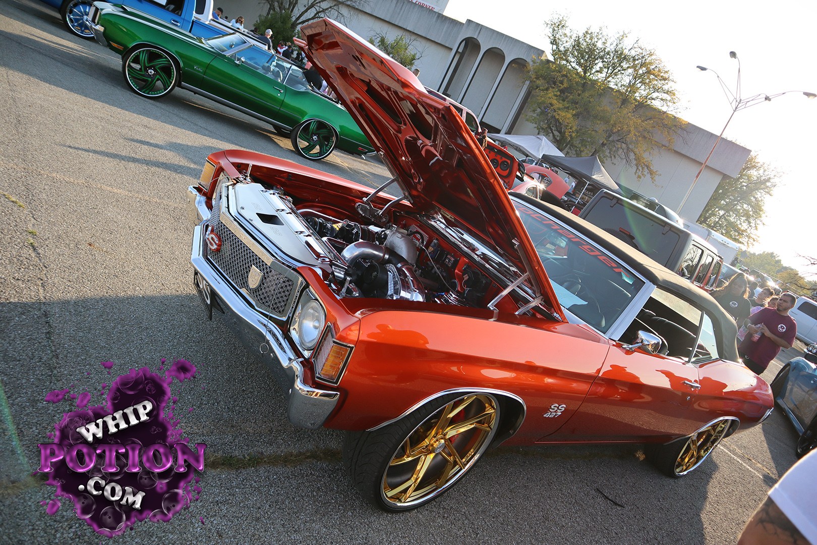 This burnt-orange Chevrolet Chevelle SS convertible brings the classic muscle with a serious custom twist, from the shiny chrome nose and cowl-induction hood to the huge gold-and-black billet-style wheels tucked under the fenders. The detailed engine bay is on full display, and the black top gives it a crisp old-school street swagger.