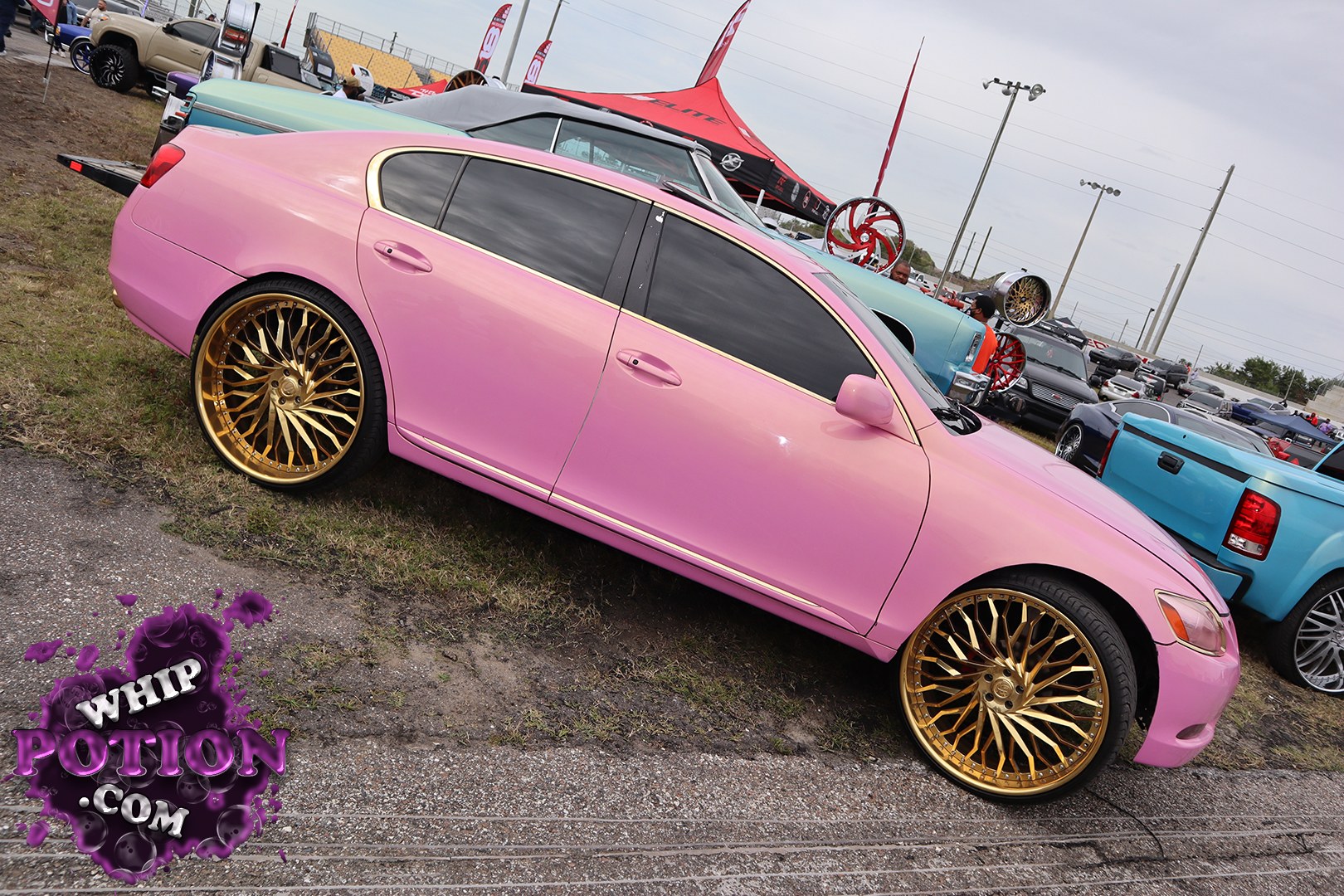 This pink four-door luxury sedan is all about clean custom style, with a smooth monochrome finish, dark tinted glass, and massive gold multi-spoke wheels tucked under the fenders. The lowered stance gives it a polished show-car look without overdoing it, and the contrast between the soft paint and aggressive rims really makes the build pop.