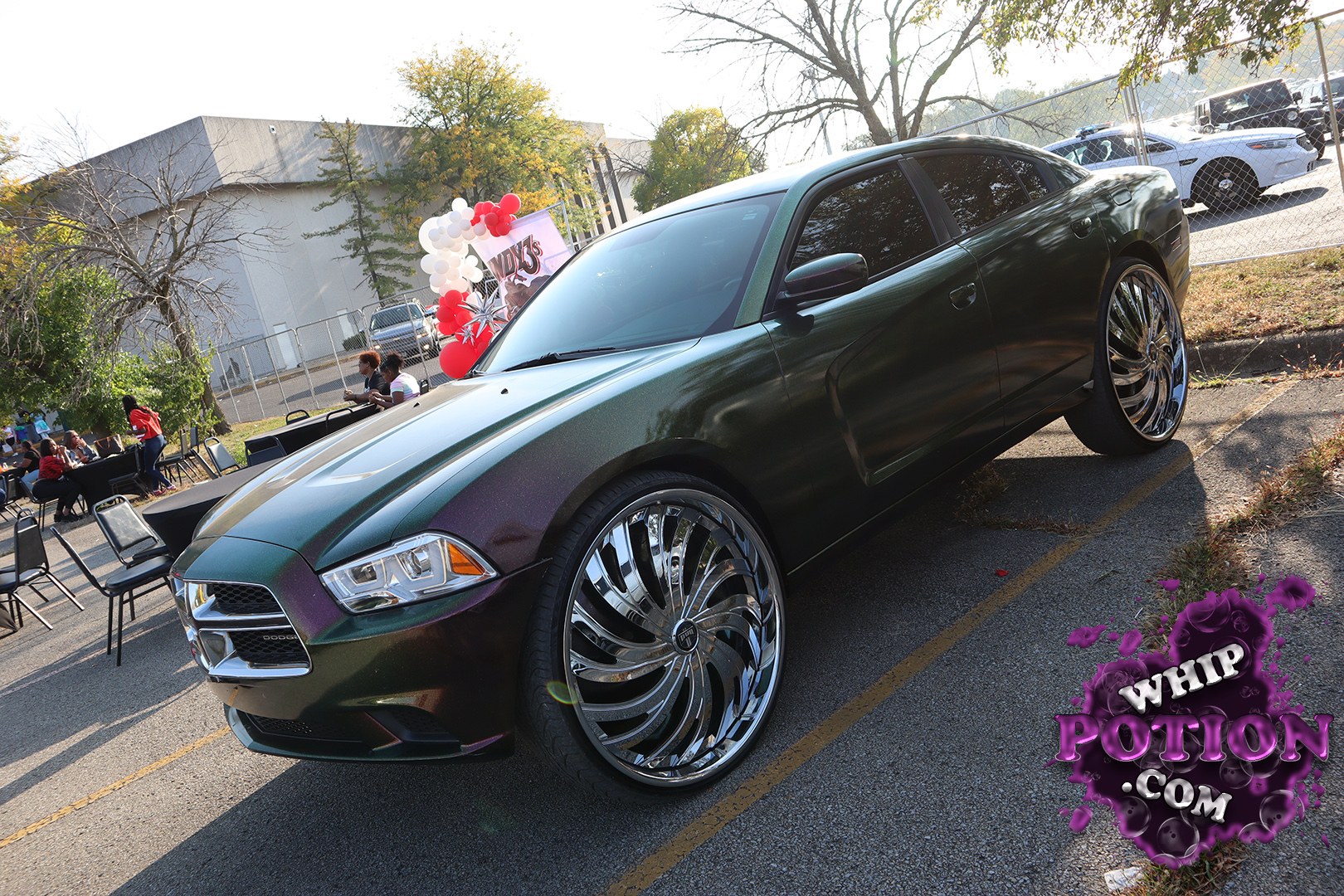 A Dodge Charger wears a deep green-to-purple flip finish that really pops over those oversized chrome swirls. The sedan sits with a clean, aggressive stance, dark-tinted windows, and a blacked-out grille that keeps the front end looking sharp. It’s a smooth custom build with just enough flash to let the wheels do the talking.