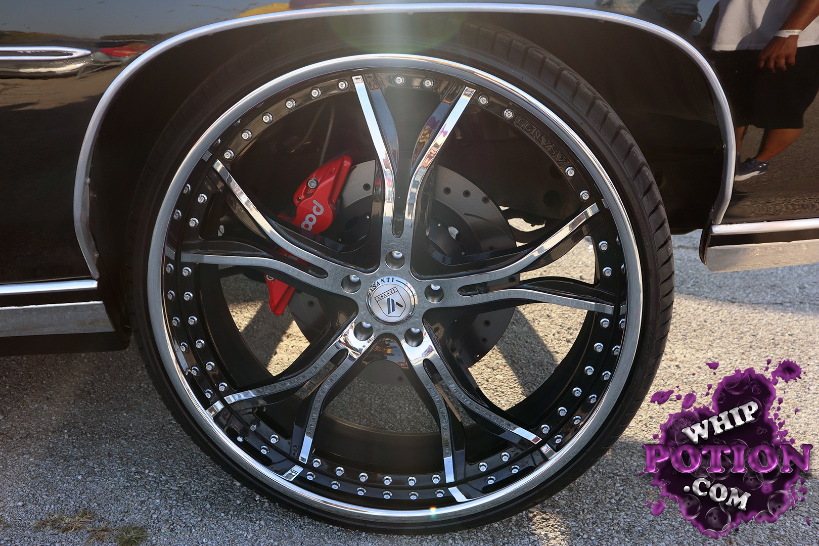 A deep-black classic cruiser sits low on massive Asanti chrome-and-black rollers, with a bright lip, exposed hardware, and big red Brembo calipers peeking through the spokes. The polished trim and clean body side molding give it a refined, old-school luxury vibe, while the wheel-and-brake combo makes it clear this one was built to be noticed.