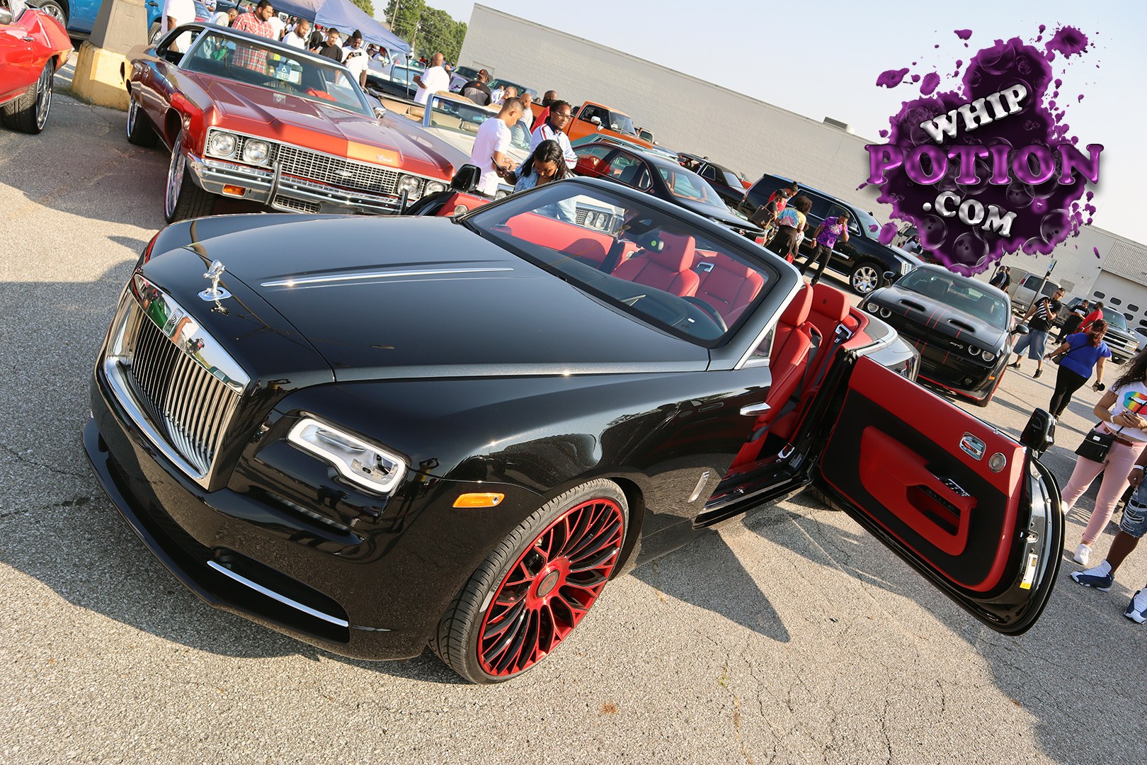 This Rolls-Royce Dawn has a serious custom vibe, with its deep black paint, bright red leather, and matching red-and-black multi-spoke wheels setting the tone. The big chrome grille, upright Spirit of Ecstasy, and coach doors give it that unmistakable Rolls presence, while the open top and bold interior color combo add a modern show-car edge.