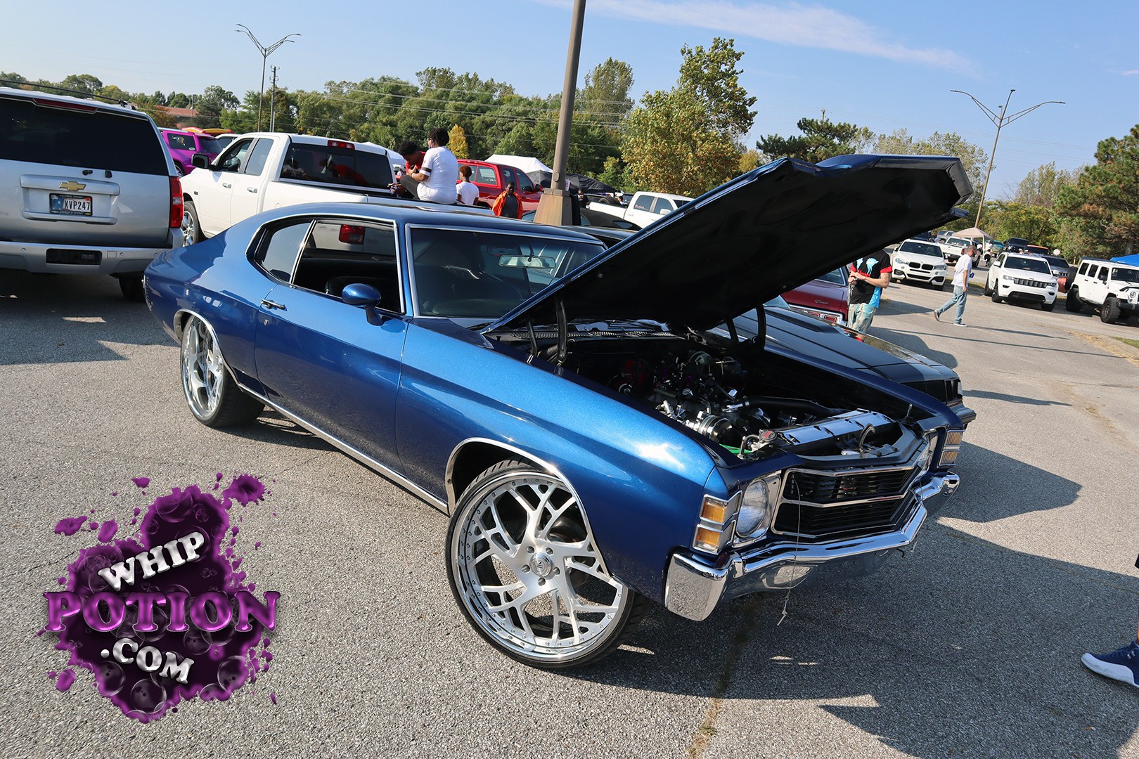 A metallic blue Chevrolet Chevelle sits mean on oversized billet wheels, with the hood up to expose a tidy engine bay that looks built with pride. The long, low body and chrome bumpers give it classic GM muscle-car presence, while the deep tint and clean stance keep it looking sharp, not overdone.