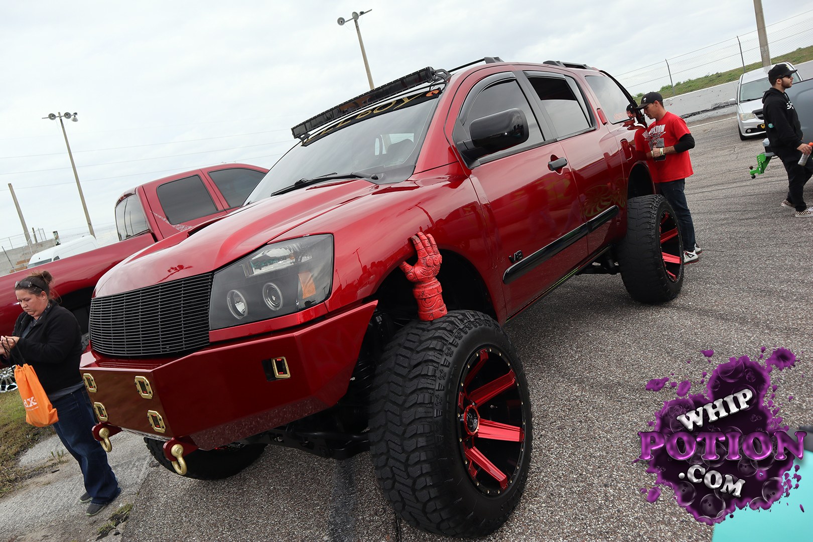 This lifted red Cadillac Escalade goes full show-truck with a shaved, custom-looking front end, oversized off-road tires, and deep red-and-black wheels. The matching red tow hooks, windshield light bar, and blacked-out trim give it a bold street-meets-trail attitude, while the high stance and clean bodywork keep it looking polished instead of overbuilt.
