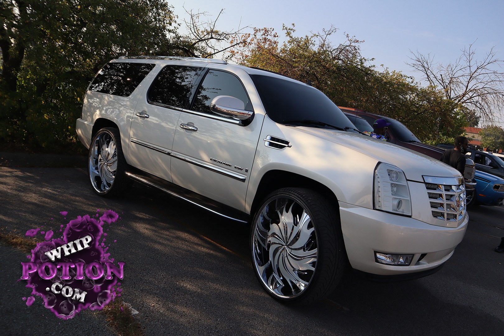 This Cadillac Escalade ESV gets a full custom treatment with pearl-white paint, massive chrome-mirror wheels, and a clean monochrome look that fits the truck’s big, boxy lines. The tinted glass, polished trim, and aggressive stance give it a properly dressed-up street presence without going over the top.