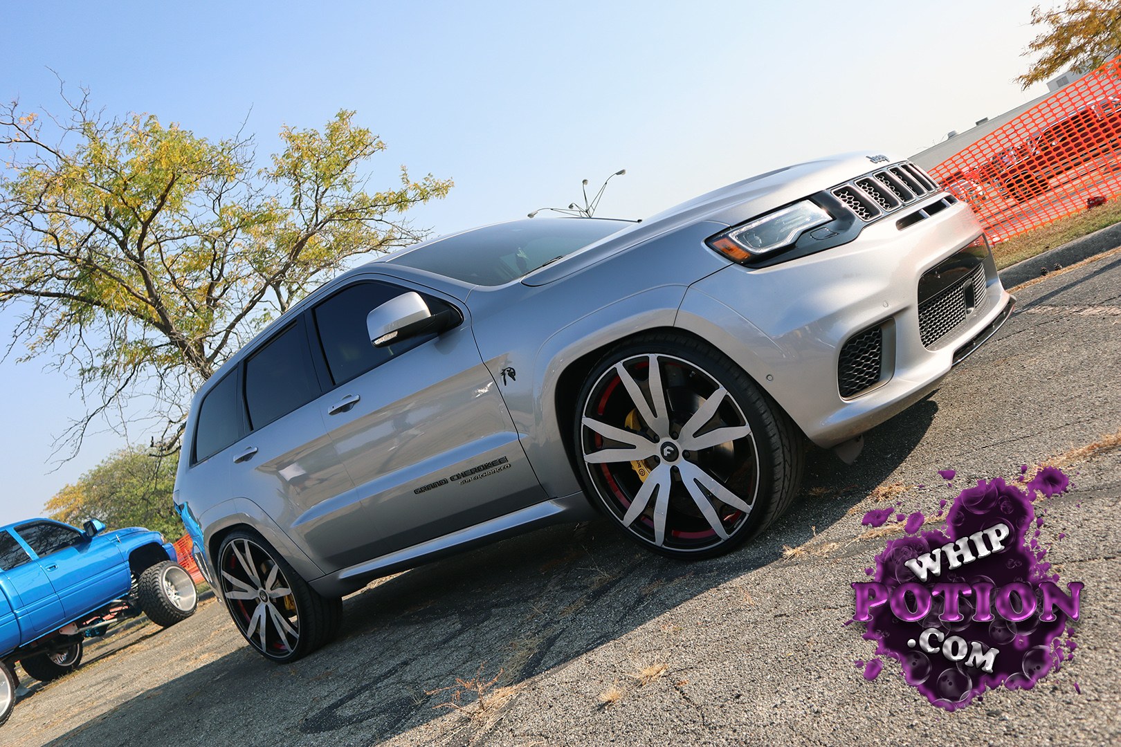 A Jeep Grand Cherokee Trackhawk gets the custom treatment with a silver finish, dark tint, and oversized two-tone wheels tucked under the arches. The lowered stance gives it a mean street look, while the black grille, hood scoop, and bright red brake calipers add just enough aggression without overdoing it.