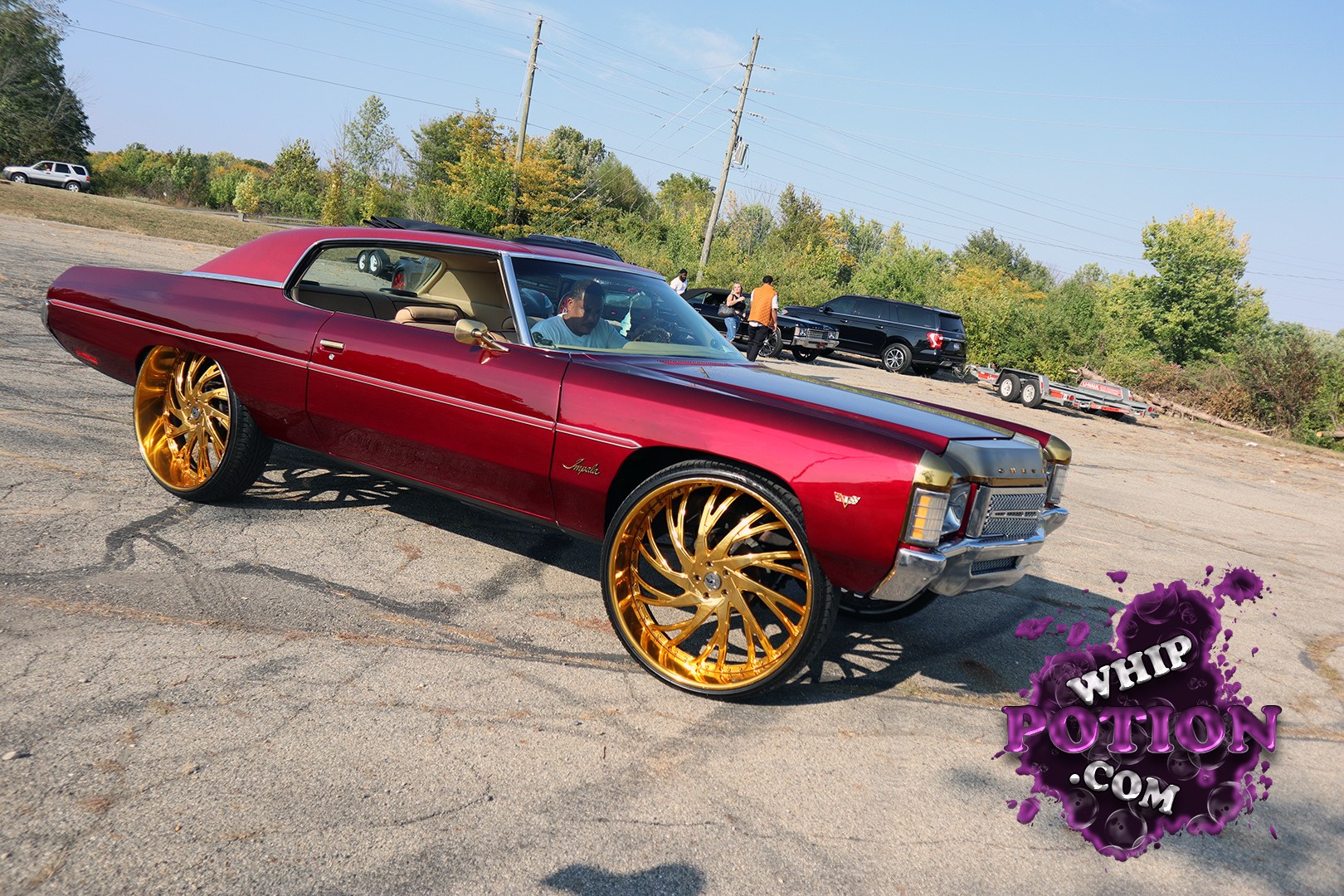 A classic Chevrolet Impala two-door with a deep burgundy finish and serious curb appeal, sitting on massive gold multi-spoke wheels that fill the wells just right. The long, low lines, chrome trim, and beige interior give it that clean old-school cruiser vibe, while the mirror-like stance makes this big Chevy look ready for a roll-through.