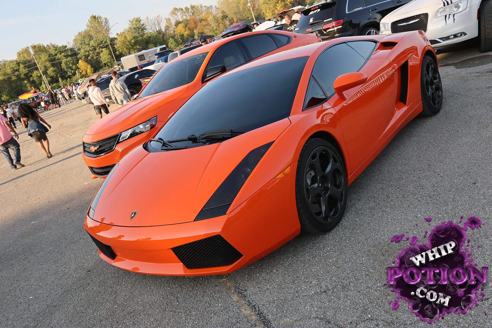 An orange Lamborghini Gallardo sits low and sharp with a stealthy black roof, tinted glass, and dark wheels that suit its wedge-shaped body perfectly. The clean nose, side intake, and jewel-like badges give it that unmistakable supercar presence, while the matching orange crossover behind it adds a nice contrast to the lineup.