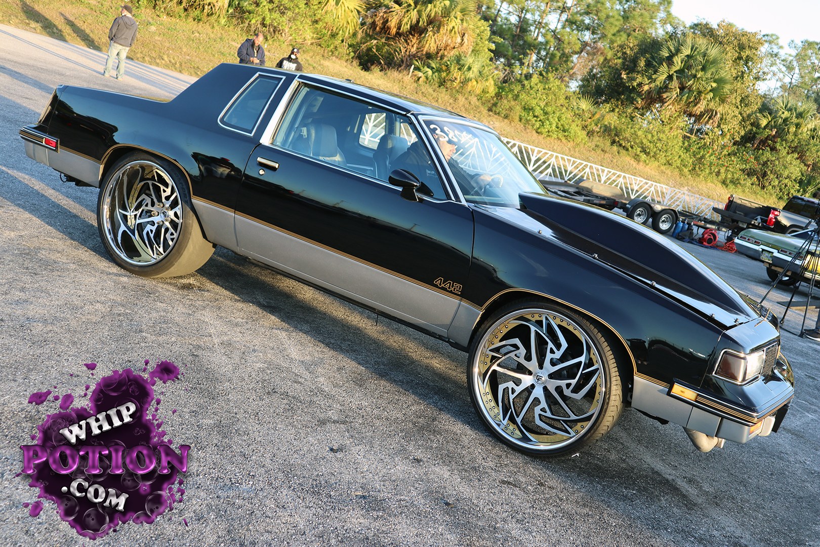 A classic Oldsmobile Cutlass 442 wears a deep black-and-silver two-tone that really suits the long, squared-off body. The big custom wheels fill the wells nicely, and the cowl hood gives it a serious street presence. Clean trim, tinted glass, and that 442 badging keep it rooted in muscle-car history while the modern stance updates the whole build.
