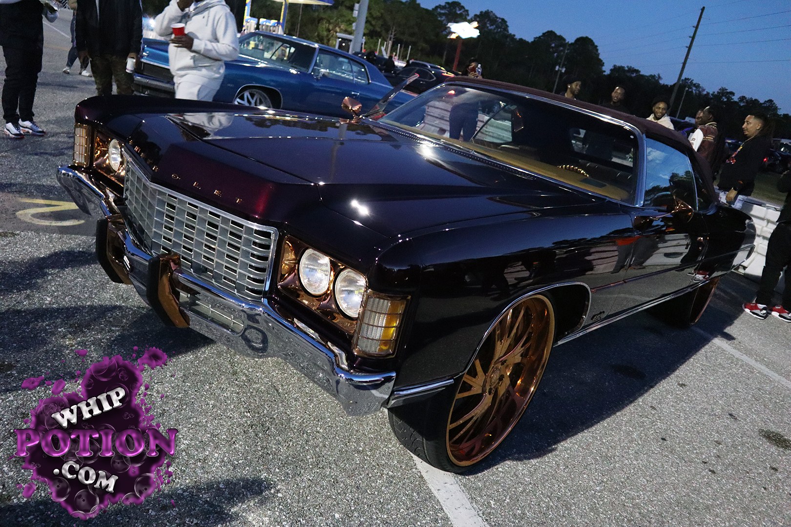 This Chevrolet Impala convertible wears a deep black finish with a maroon top and a bold chrome grille that gives it plenty of old-school presence. The big copper/gold wheels fill the wells nicely, and the clean lowered stance ties the whole build together without overdoing it. It’s a sharp, well-finished cruiser with serious street appeal.