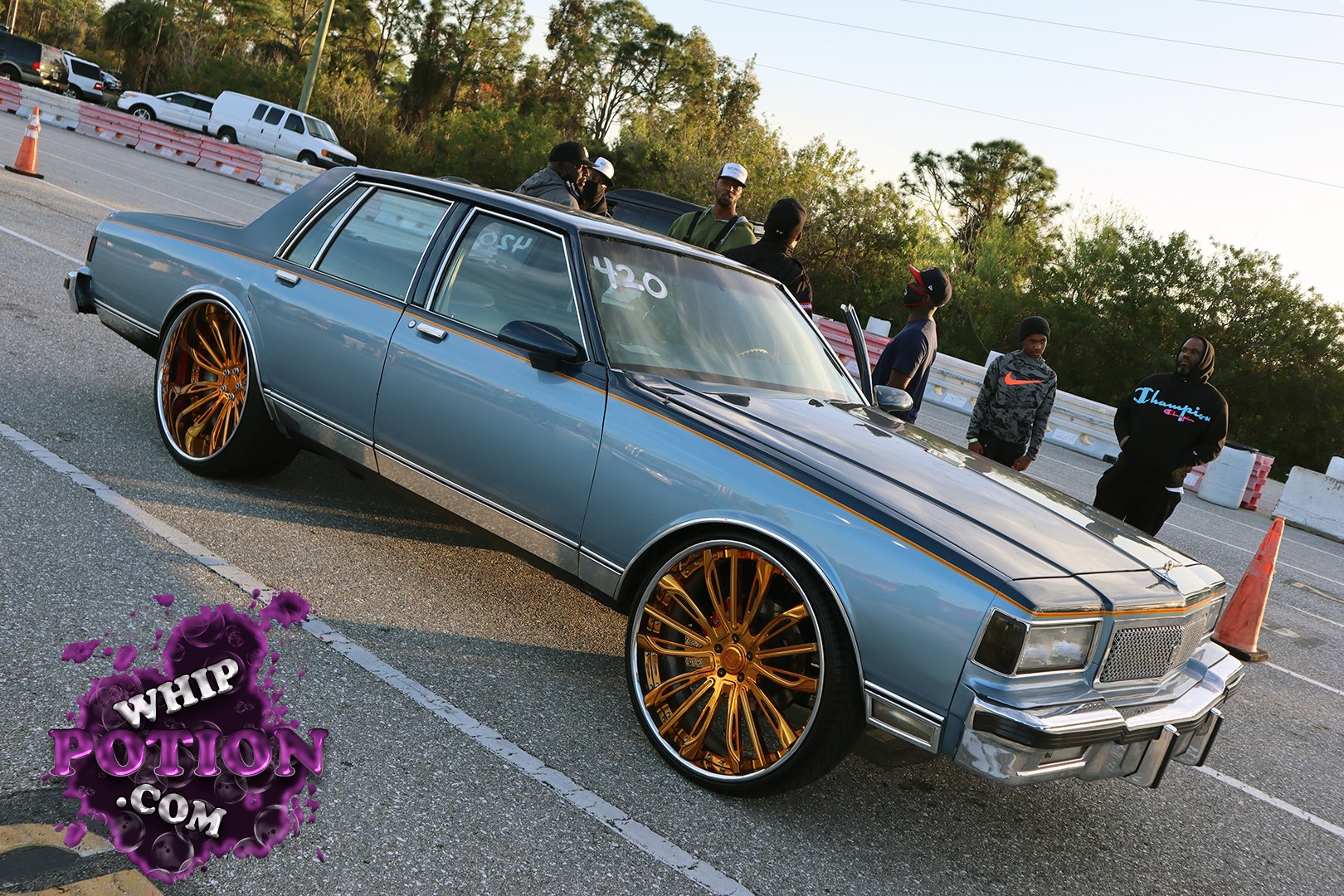 This classic Chevrolet sedan has that clean old-school presence, wearing a powder-blue finish with a thin gold pinstripe and a black hood for contrast. The huge gold multi-spoke wheels with skinny low-profile tires give it a modern big-wheel look, while the chrome bumpers and square body lines keep the vintage luxury vibe intact.