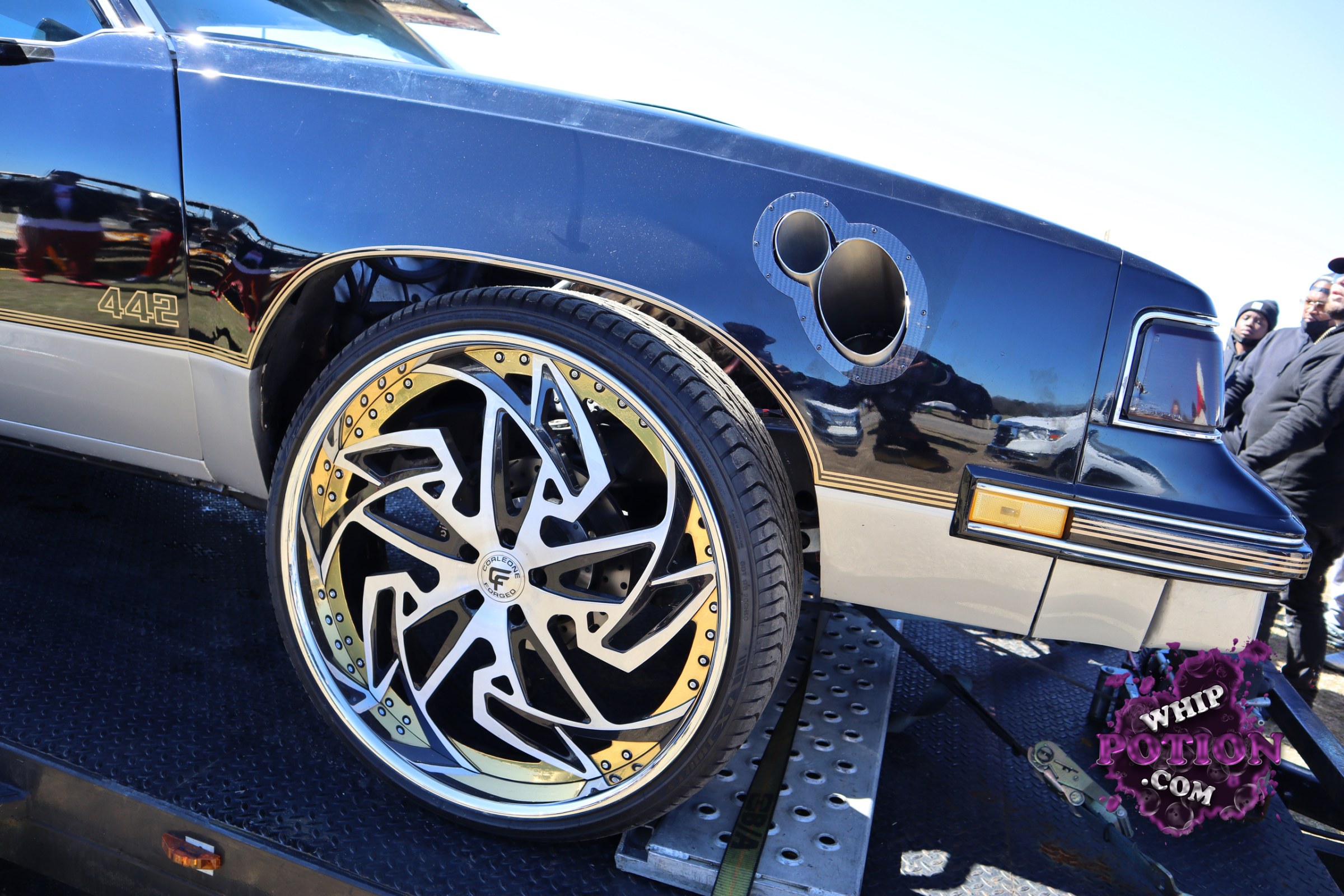This classic Oldsmobile Cutlass 442 wears a crisp black-and-silver two-tone with gold pinstriping and the 442 callout set into the front fender. The big staggered billet-style wheels, low-slung stance, and open hood cutout give it a hard-edged custom look, while the factory body lines and trim keep the muscle-era identity front and center.