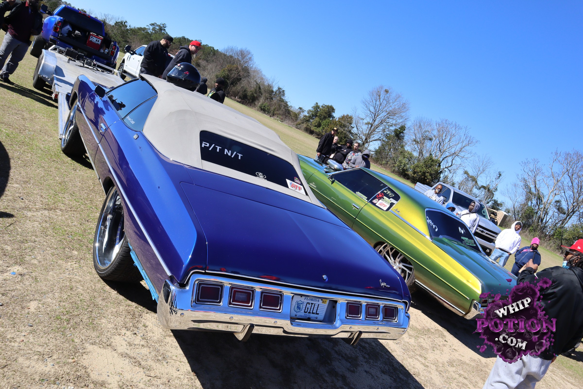 Two classic Chevy Impalas sit low and long with their tops down under the covers, one in deep blue with chrome bumpers and the other in a wild green-to-gold fade. Big polished wheels fill the wells, and the clean, color-matched builds have that well-sorted street-cruiser look that makes full-size Bowties so hard to ignore.