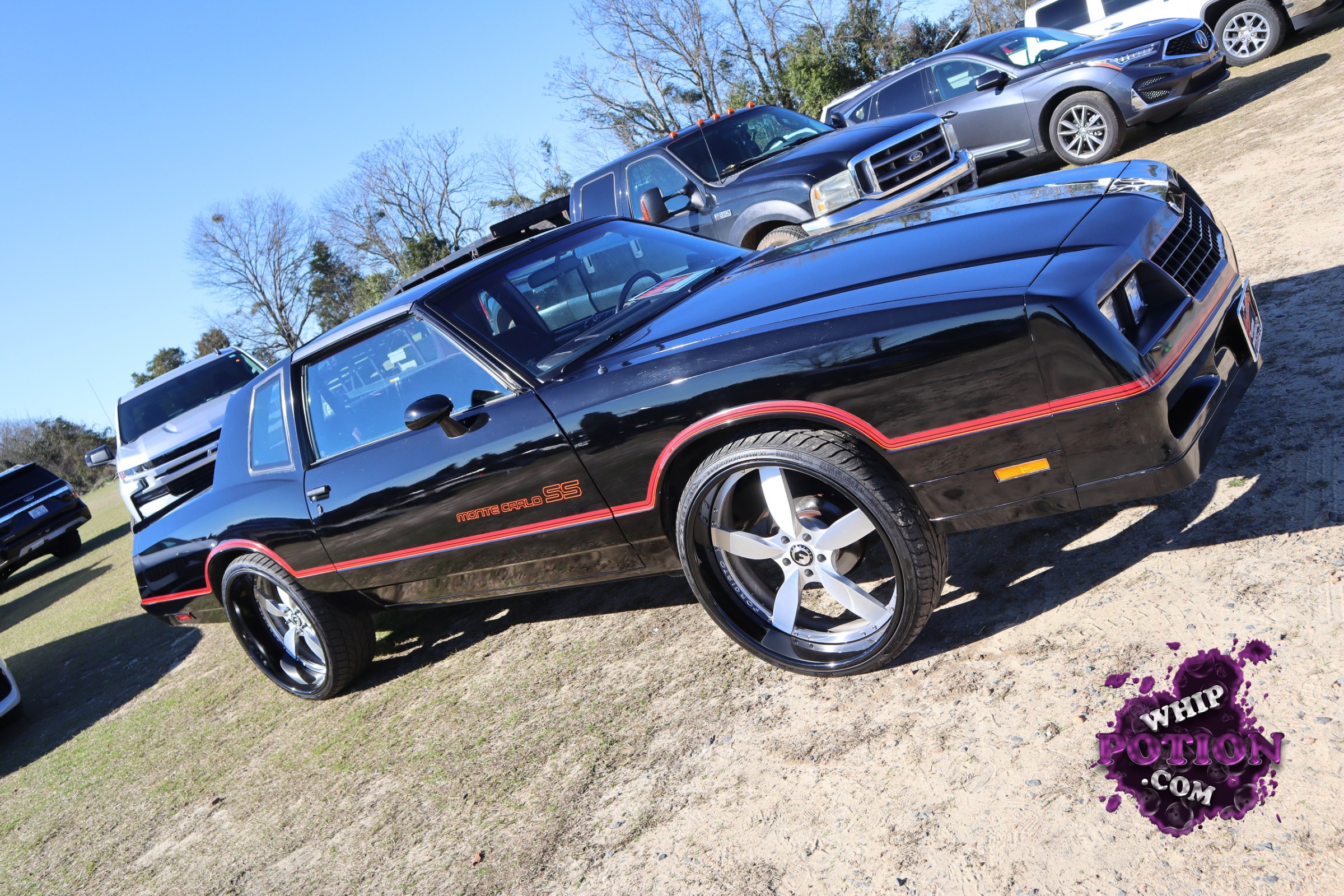A black Chevrolet Monte Carlo SS sits on oversized five-spoke wheels with a clean, nose-high stance that gives it a bold street presence. The red pinstriping and matching SS badging play nicely against the glossy paint, while the long coupe profile and dark-tinted glass keep the whole build looking tight and purposeful.
