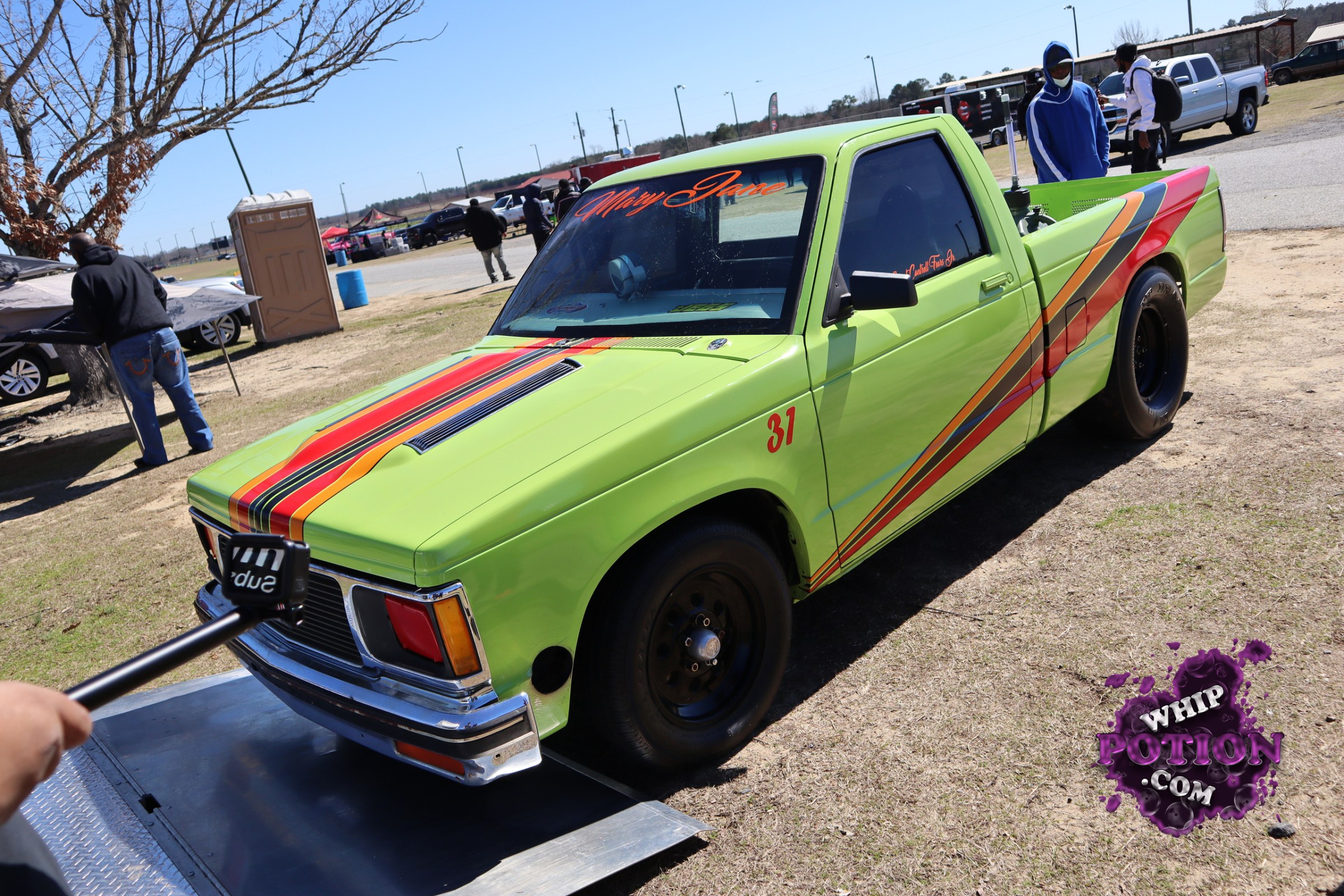This lime-green compact pickup has a wild ’70s-inspired vibe, with bold retro striping sweeping over the hood, cab, and bed. The black steel wheels and fat rear tires give it a purposeful stance, while the custom window banner and numbered door marking add a race-truck touch. It’s a clean, eye-catching build with plenty of attitude.