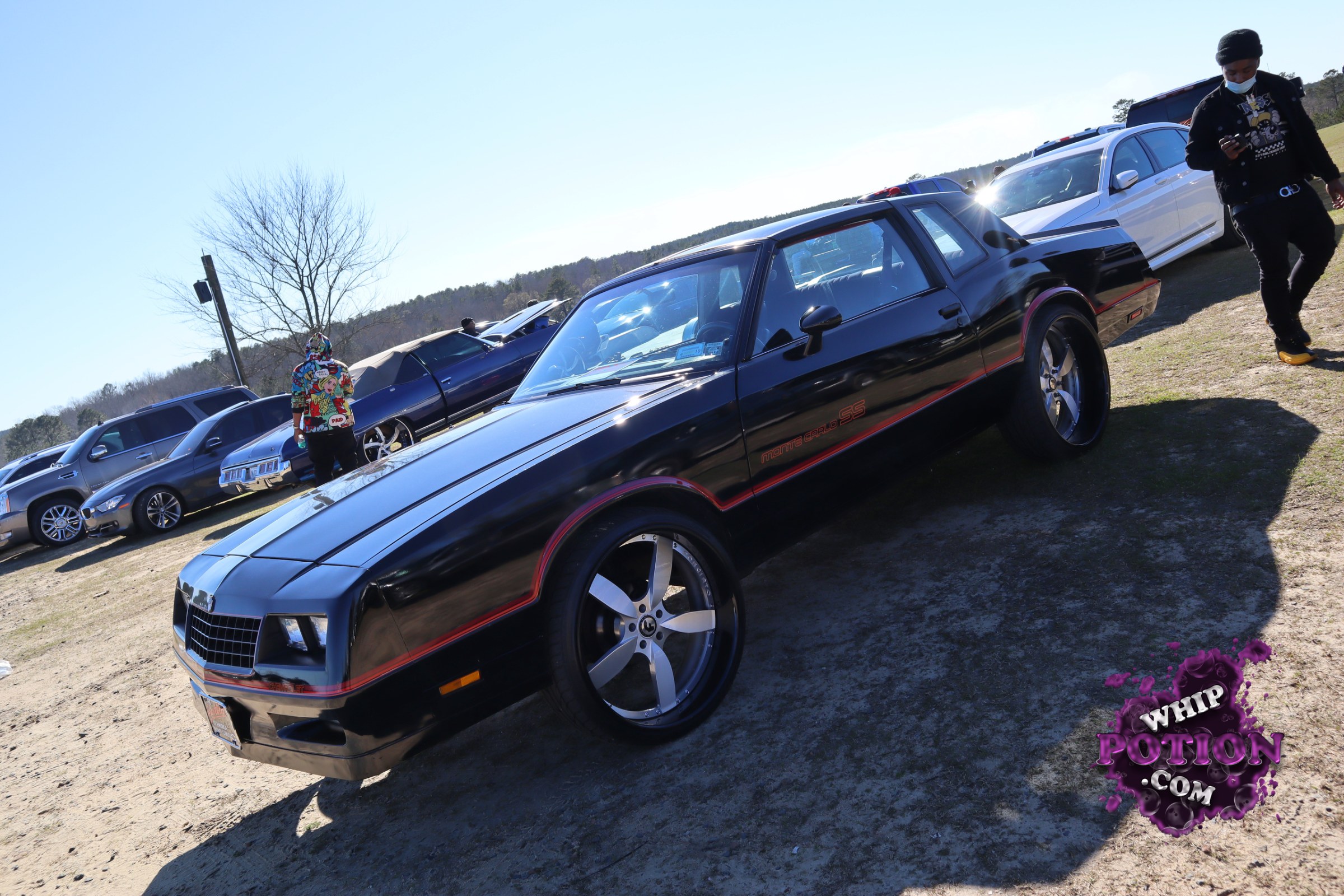 A black Monte Carlo SS with a clean, murdered-out look and a subtle red pinstripe, sitting on big five-spoke chrome wheels with serious sidewall stretch. The long hood, square nose, and SS badging give it that classic G-body swagger, while the low stance and glossy finish keep it looking sharp and well sorted.