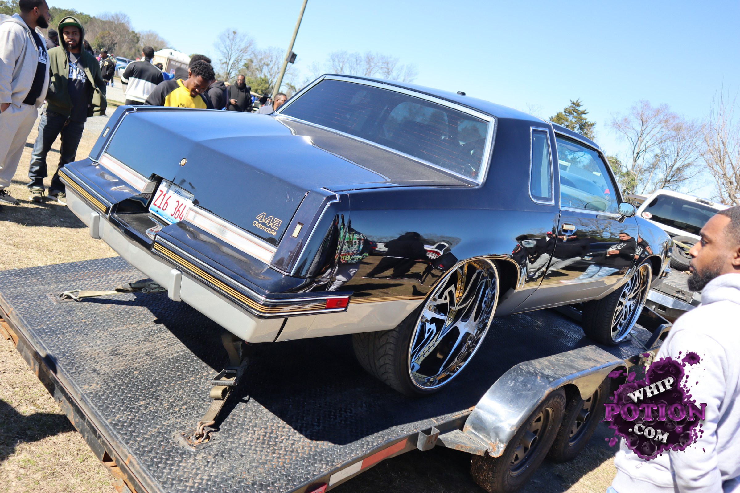 This black-and-silver Oldsmobile 442 wears a hard-edged custom look, with a mirror-gloss finish, deep-dish billet-style wheels, and a tucked stance that gives it real presence on the trailer. The long coupe body and crisp 442 badging keep it rooted in muscle-car territory, while the oversized rims push the whole build into modern show-car style.