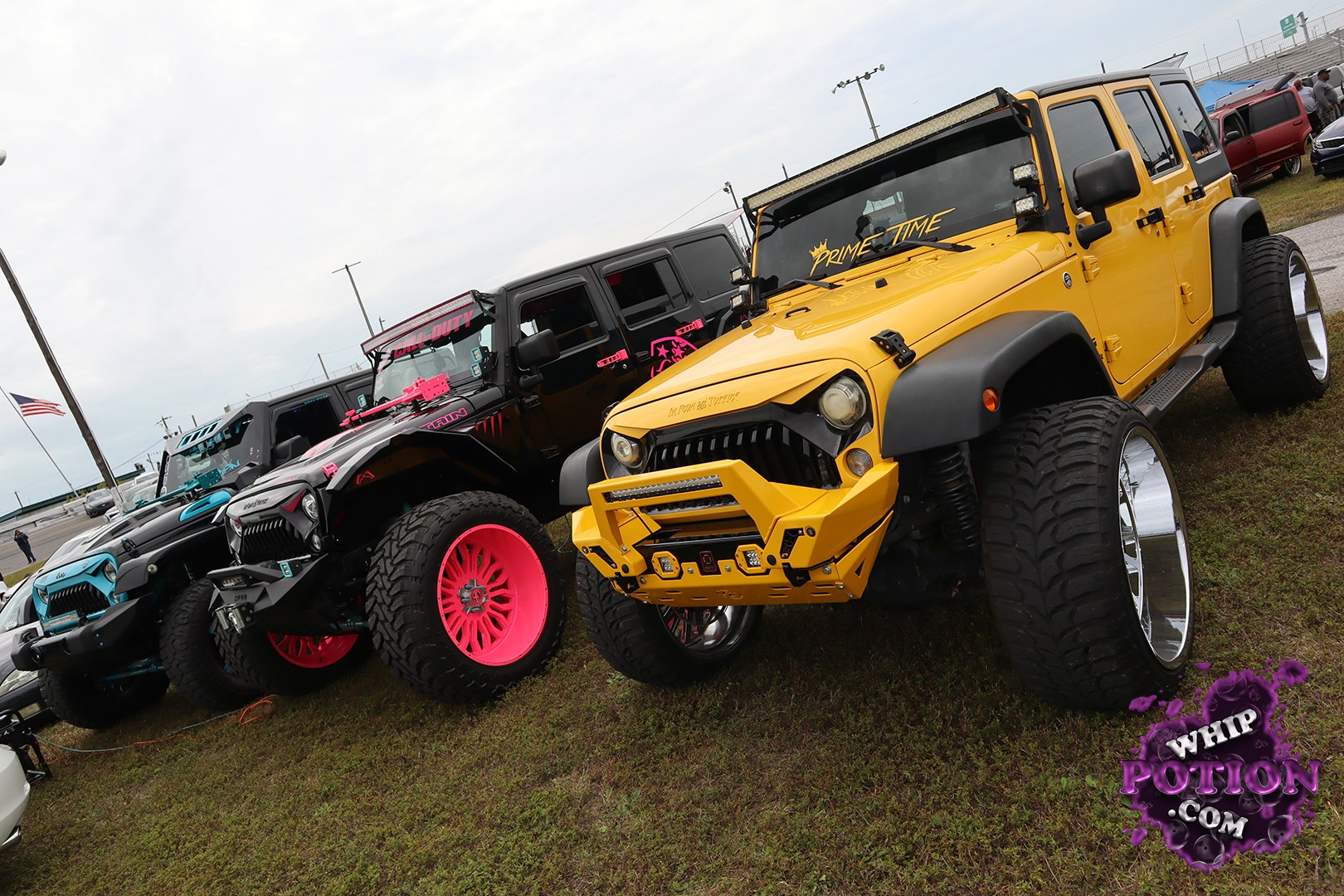 A trio of custom Jeep Wranglers sits on massive big-wheel setups, each one pushed hard into show-truck territory with wild paint, huge offsets, and heavy aftermarket armor. The yellow four-door leads the pack with a raked stance, deep-dish chrome wheels, and a brutal front bumper, while the black builds bring bright neon accents and plenty of attitude.