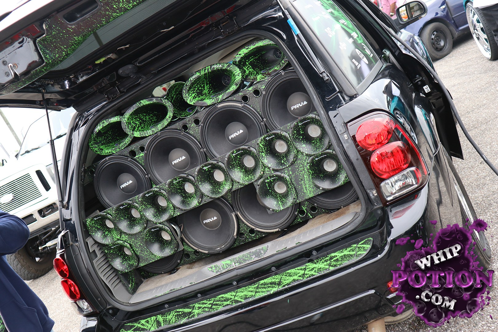 This black custom SUV is built for straight-up bass, with the hatch packed full of PRV speakers, multiple subwoofers, and a wild black-and-neon-green splatter theme. The rear glass and trim carry the same look, while the taillights and bodywork keep the exterior clean and factory-based. It’s a serious audio build with real show-car attitude.