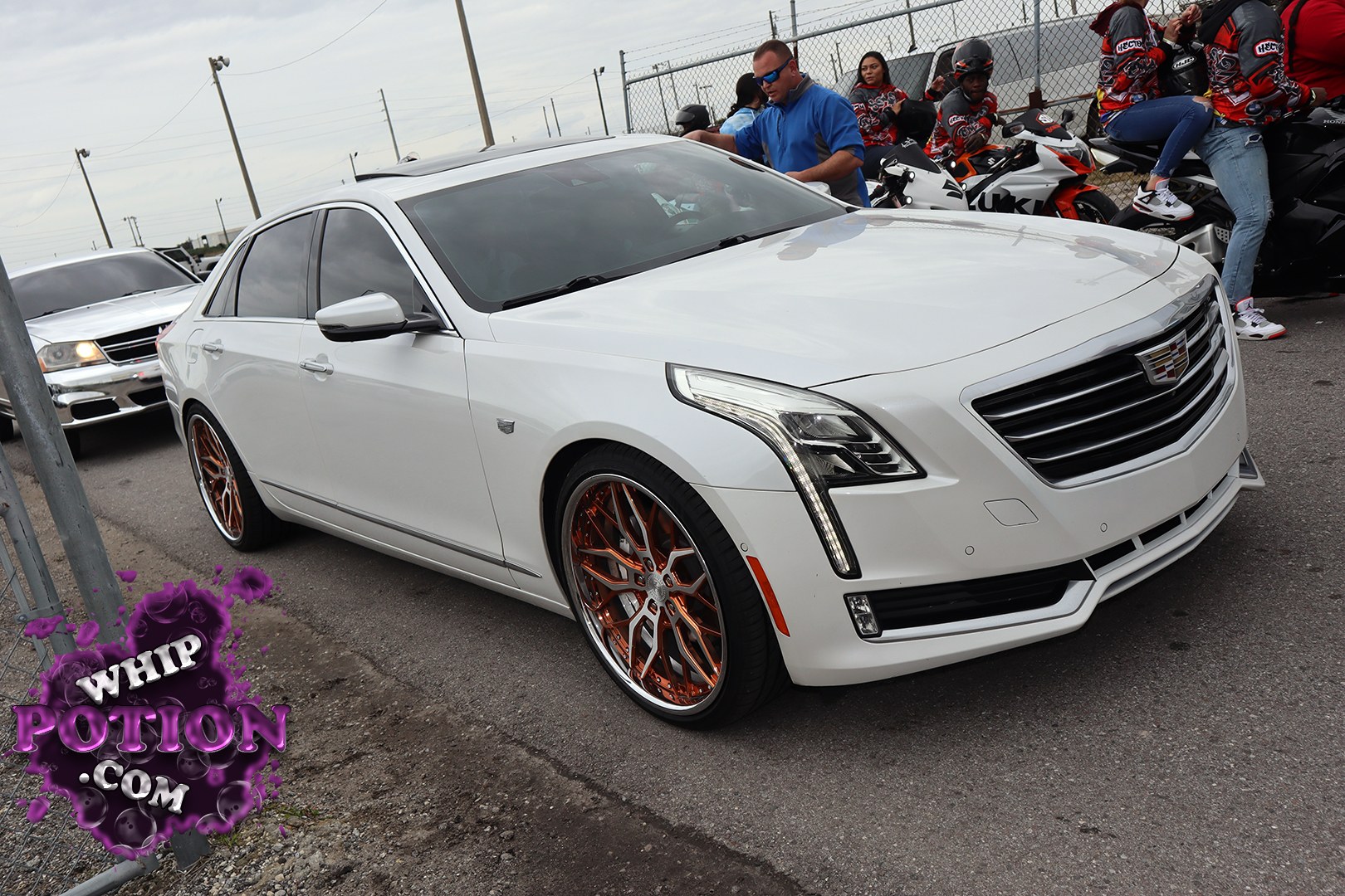 A clean white Cadillac sedan sits low on copper-and-chrome multi-spoke wheels, giving the big luxury body a sharp custom edge without going overboard. The vertical LED lighting, bold grille, and tinted glass keep it looking modern, while the staggered wheel fitment and polished lip add just enough show-car flavor for a proper street build.