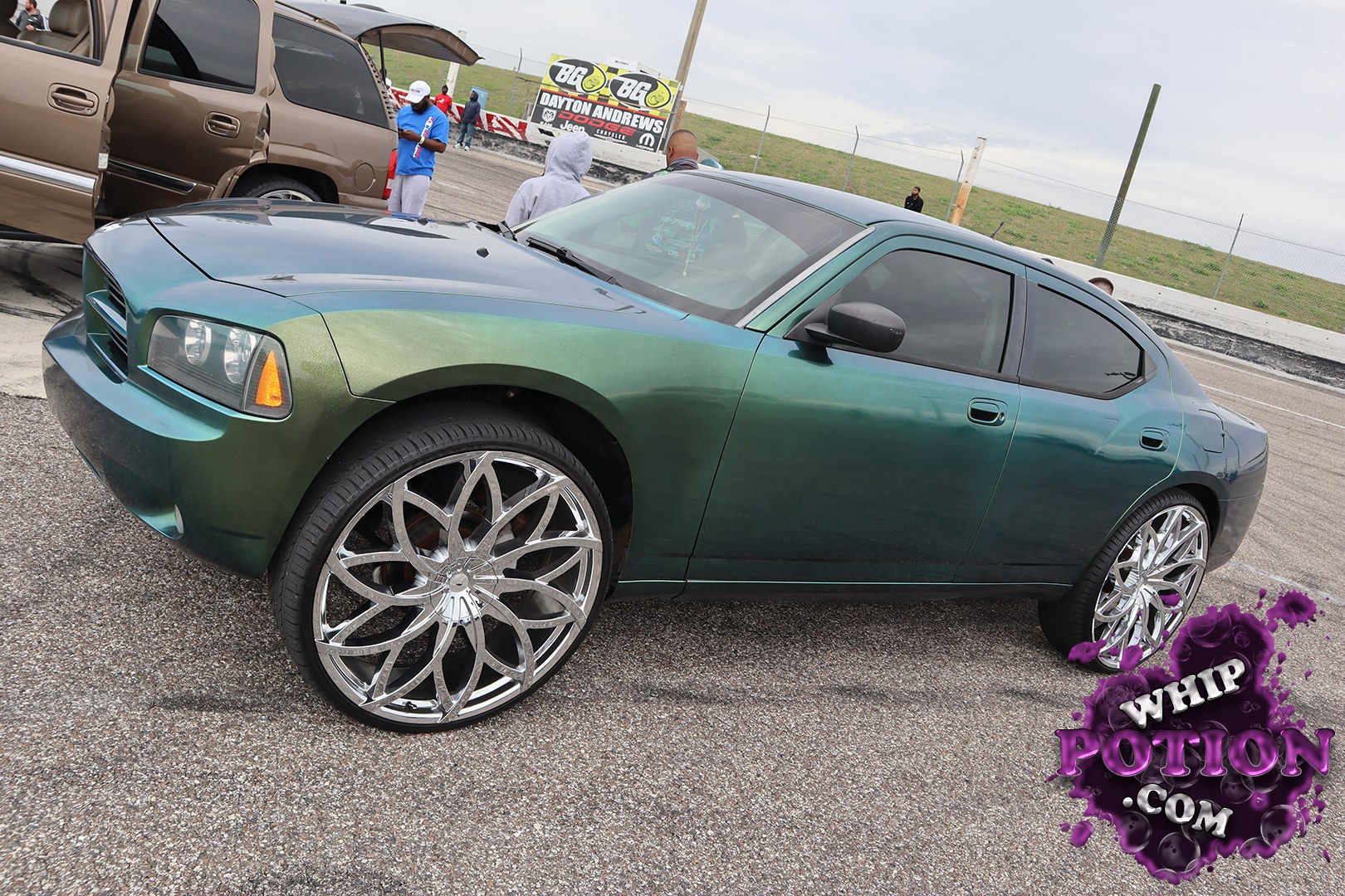 This Dodge Charger gets a serious custom touch with a deep green-to-blue chameleon finish and massive polished multi-spoke wheels tucked under the fenders. The stance is clean and aggressive without going overboard, and the dark-tinted glass and shaved-look smooth bodywork give it that polished street-machine vibe.
