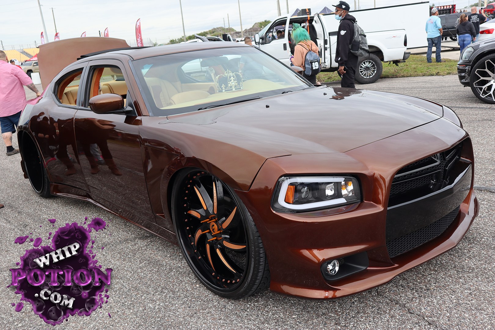 A Dodge Charger with a deep brown finish sits slammed over huge black-and-orange custom wheels, giving it that mean, tailored street-machine look. The shaved, smoothed bodywork and smoked grille keep the front end clean, while the tan interior adds a classy contrast. It’s got the stance and presence of a serious custom build without overdoing the details.