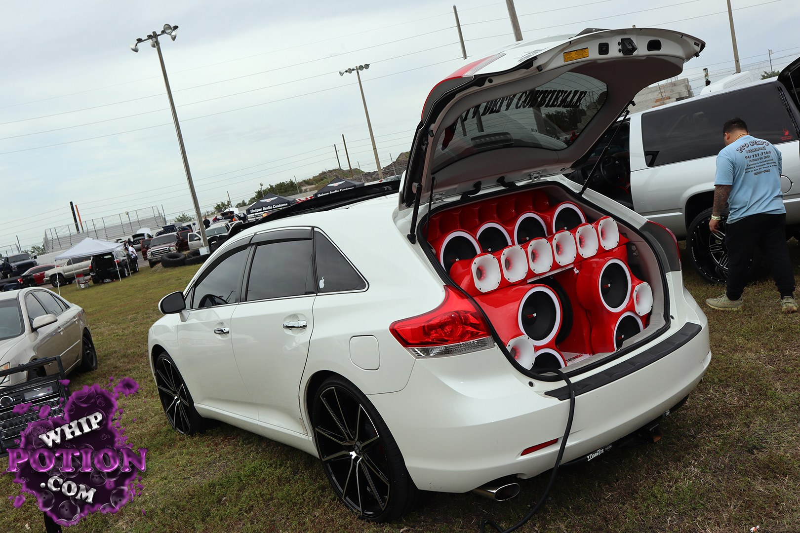 A white SUV, likely a Toyota Venza based on the taillight and side profile, gets the full custom-audio treatment with the hatch packed wall to wall in a red-and-white speaker array. The big black multi-spoke wheels and tinted glass keep the outside clean, but the real story is all business in the cargo area.