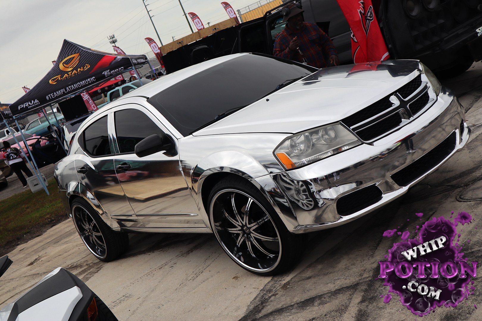 A Dodge Avenger gets a full chrome-dipped look that’s impossible to miss, backed by tinted glass, a shaved-clean body, and big black multi-spoke wheels with polished lips. The oversized stance gives it a custom show-car attitude without overdoing the drop, and the mirrored finish throws back every bit of the surrounding scene in wild fashion.
