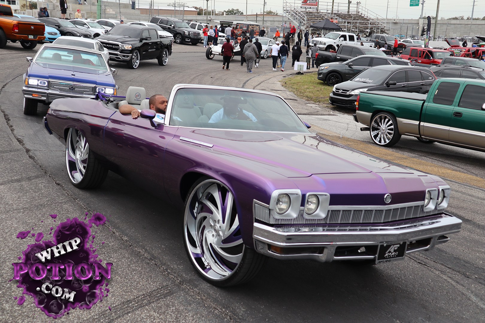 A deep purple Buick convertible glides through the MLK Weekend lineup at Showtime Speedway, riding on massive custom billets that fit the car’s long, low profile perfectly. The chrome grille and stacked headlights keep the vintage Buick face intact, while the white interior and clean drop-top setup give it that polished boulevard-cruiser feel car show folks appreciate.