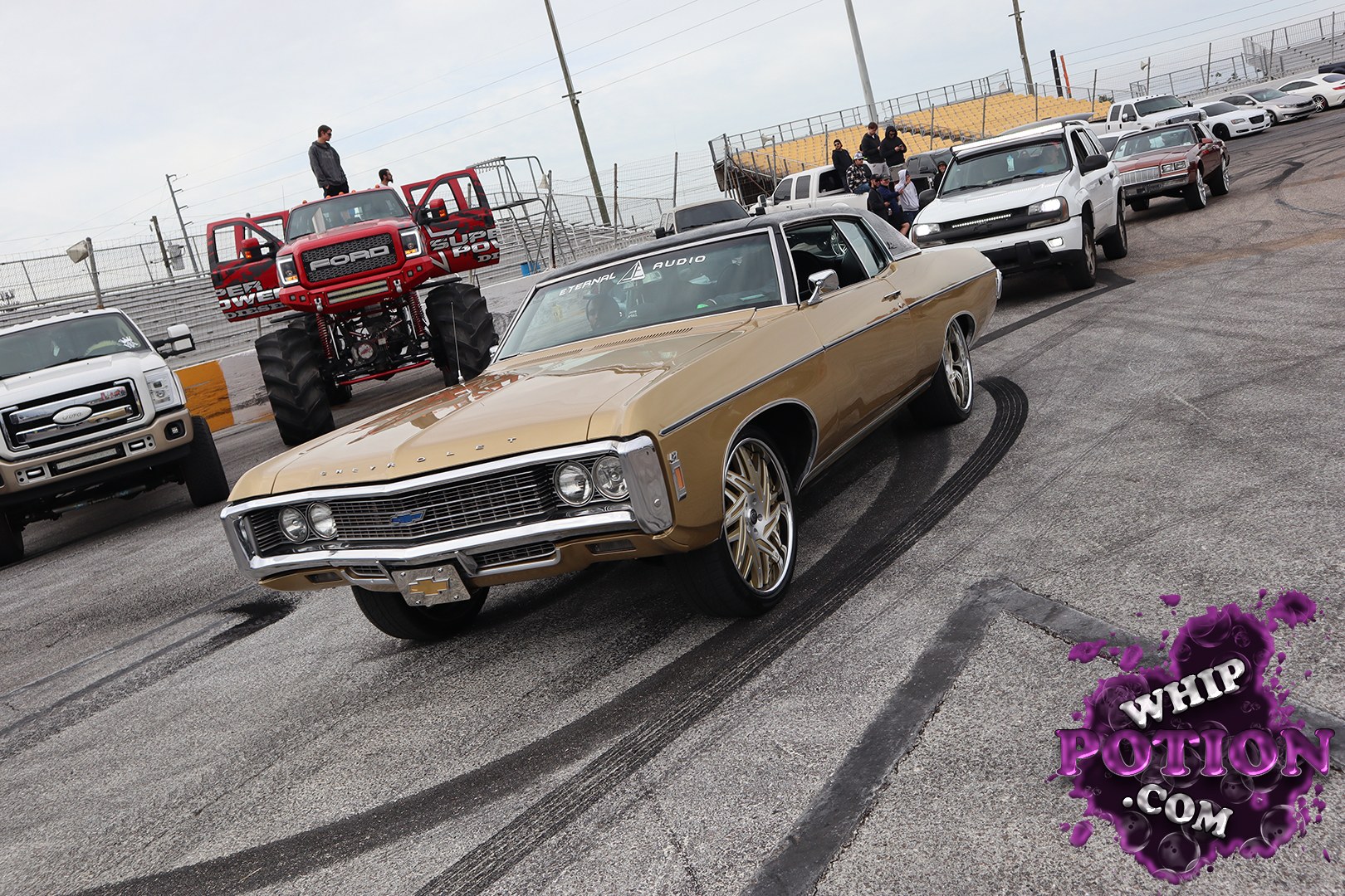 A classic Chevrolet Chevelle coupe gets a clean custom touch with its tan-and-gold paint, big chrome grille, and oversized multi-spoke wheels tucked under the fenders. The tall sidewall front tire and the rear stance give it that proper pro-street attitude, while the windshield banner and blacked-out top keep it feeling street-savvy rather than overbuilt.
