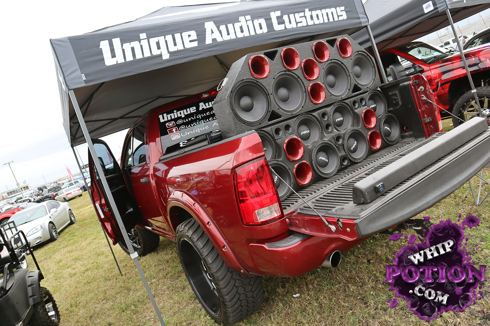 This red full-size pickup is built for sound, with the bed stuffed by a towering wall of PRV speakers and red horn drivers under the canopy. The wide black wheels and chunky off-road tires give it a tough, lifted look, while the smoked rear lamps and shaved-down tailgate area keep the custom theme clean and mean.