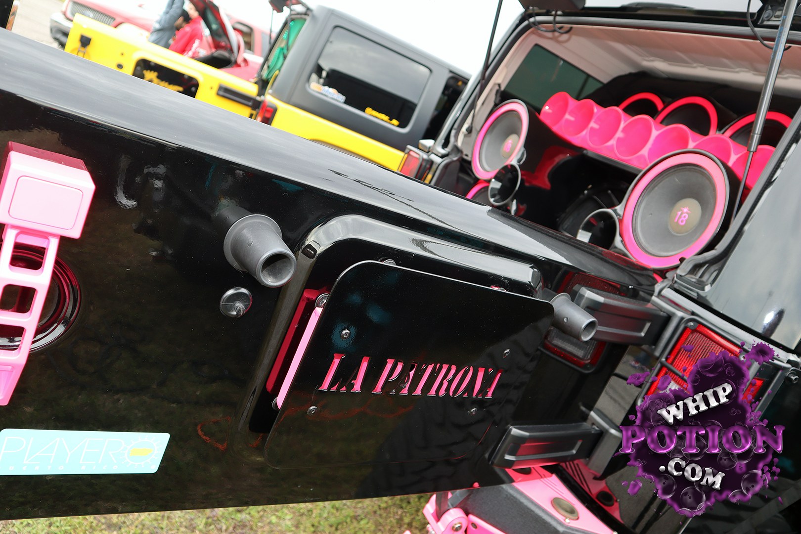 A heavily customized Jeep Wrangler shows off a wild black-and-pink theme, with the tailgate turned into a rolling sound stage and huge pink-ringed speakers packed into the cargo area. The “LA Patrol” panel, matching accents, and clean shaved bodywork give it a show-truck attitude that’s equal parts tough and flashy.