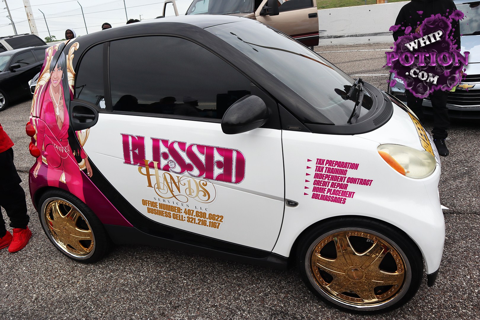 A tiny Smart Fortwo gets a full custom treatment here, with white-and-black paint, bold “BLESSED” side graphics, and gold billet-style wheels that give it a flashy show-car vibe. The tinted glass, wraparound artwork, and slammed little footprint make it feel more like rolling promo art than basic commuter transport.