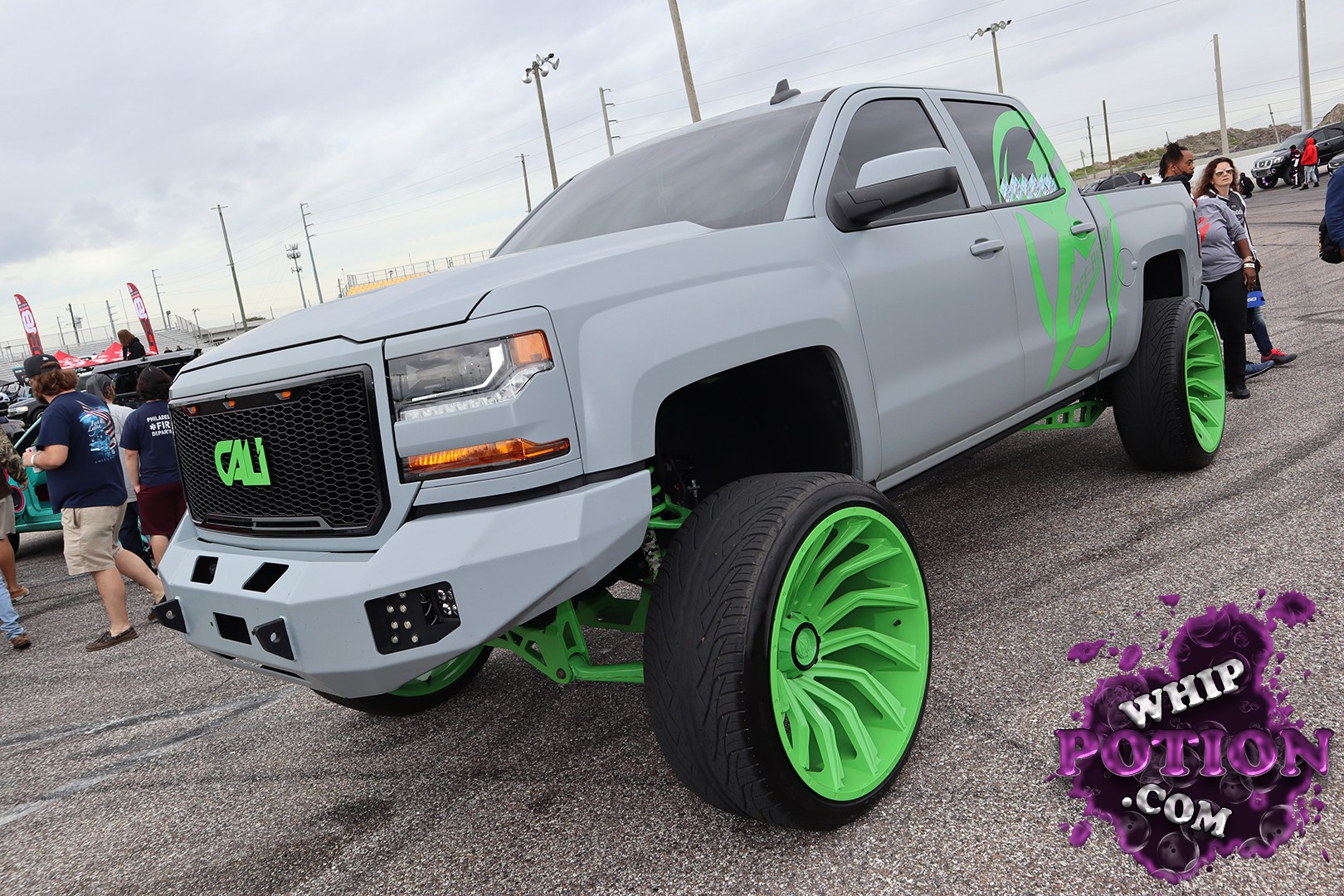This lifted Chevrolet Silverado has a wild custom street-truck look, finished in matte gray with neon green accents that really pop against the body and grille. The oversized green wheels, low-profile tires, and exposed suspension hardware give it a serious show build vibe, while the sharp body kit and tinted glass keep it clean and aggressive.