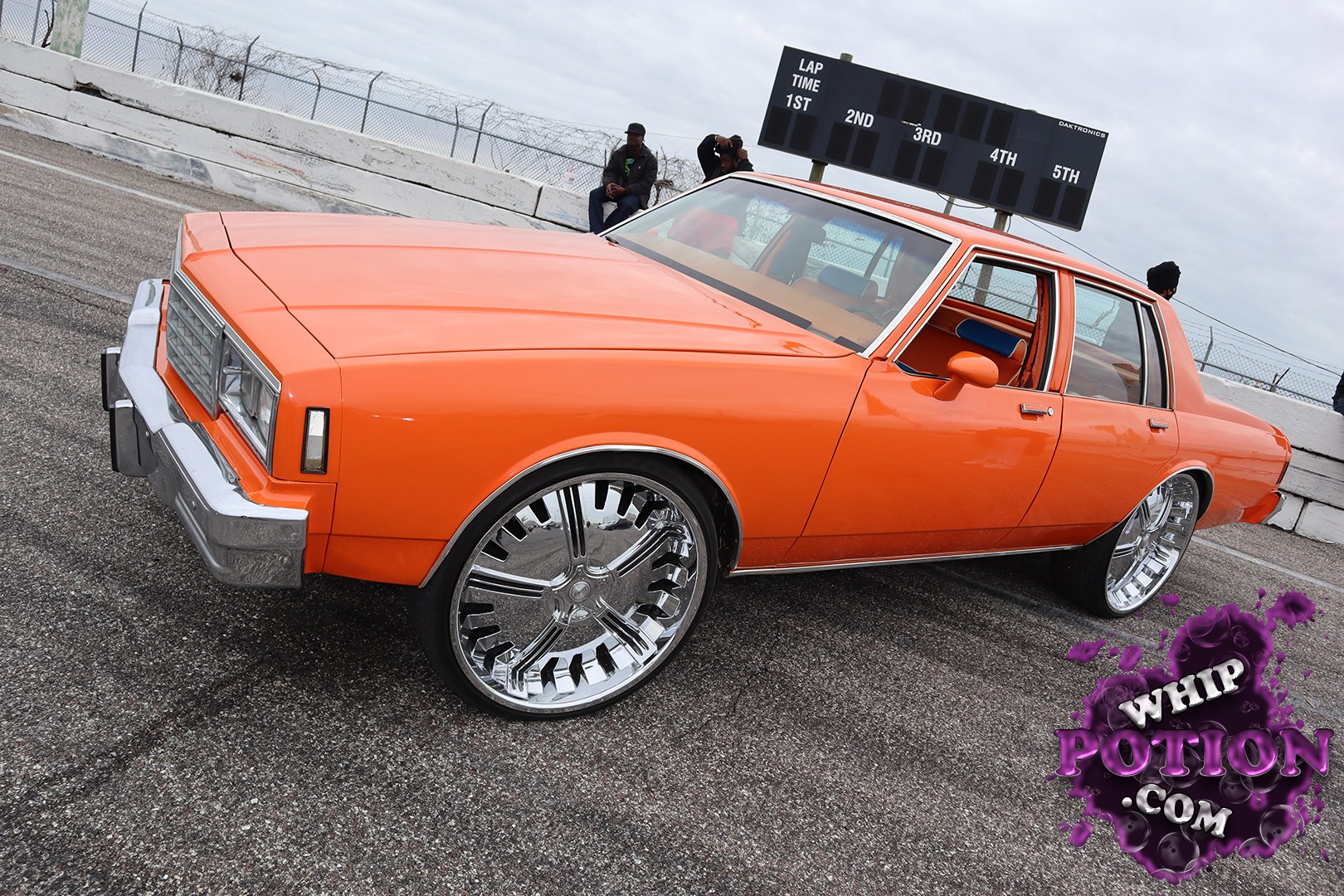This orange four-door muscle sedan has a hard-to-miss old-school GM profile, with a boxy nose, rectangular headlights, and chrome trim that give it that late-’70s land yacht attitude. The giant chrome wheels and low stance push the build into full custom territory, and the bright orange interior ties the whole package together with a bold, show-ready finish.