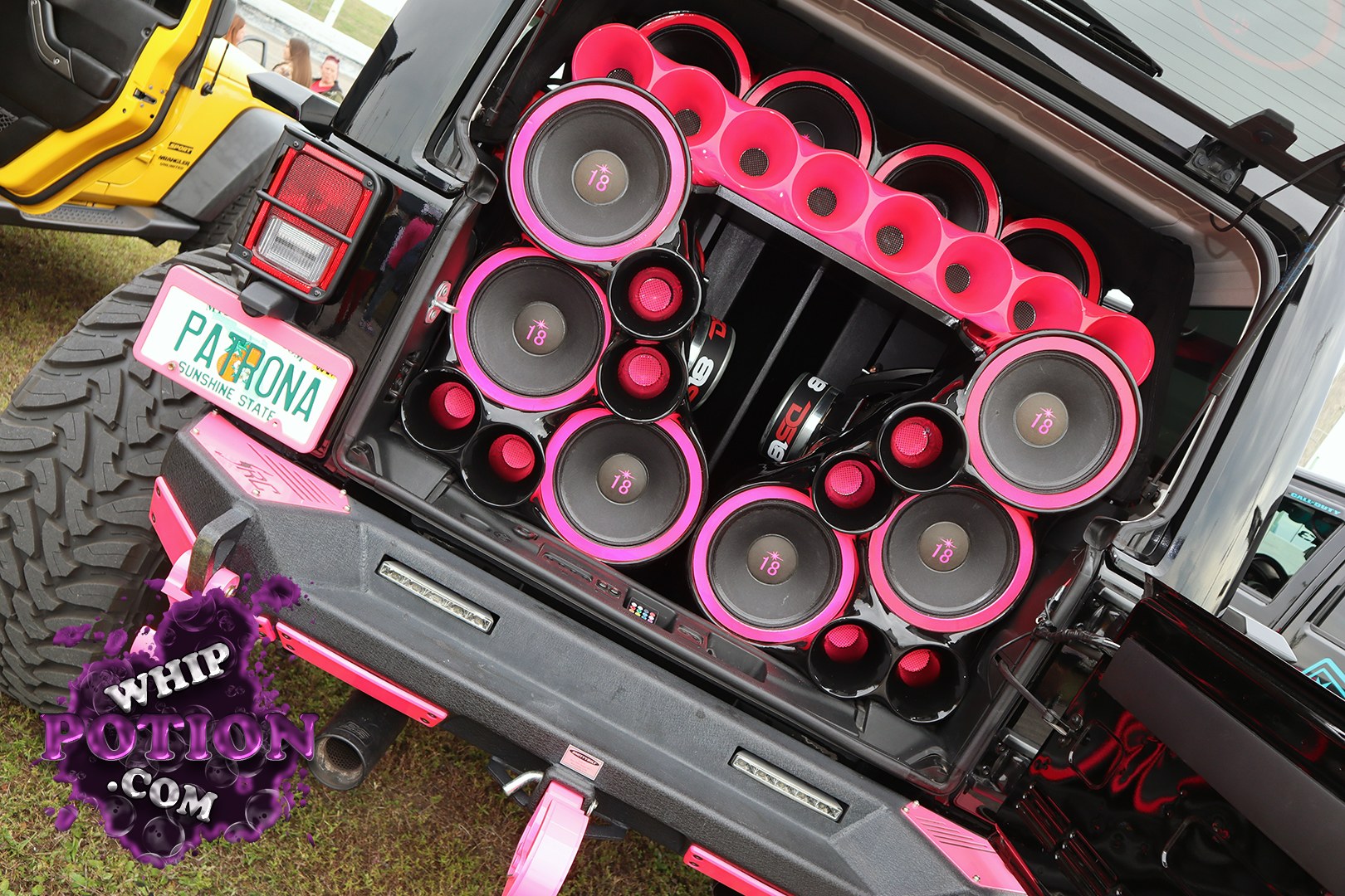 This Jeep Wrangler has been turned into a rolling bass wall, with the rear packed full of pink-ringed subwoofers and matching horn speakers built into a glossy custom enclosure. The black-and-pink theme carries through the tailgate area, while the big off-road tire and upright body keep it looking every bit like a serious show rig.