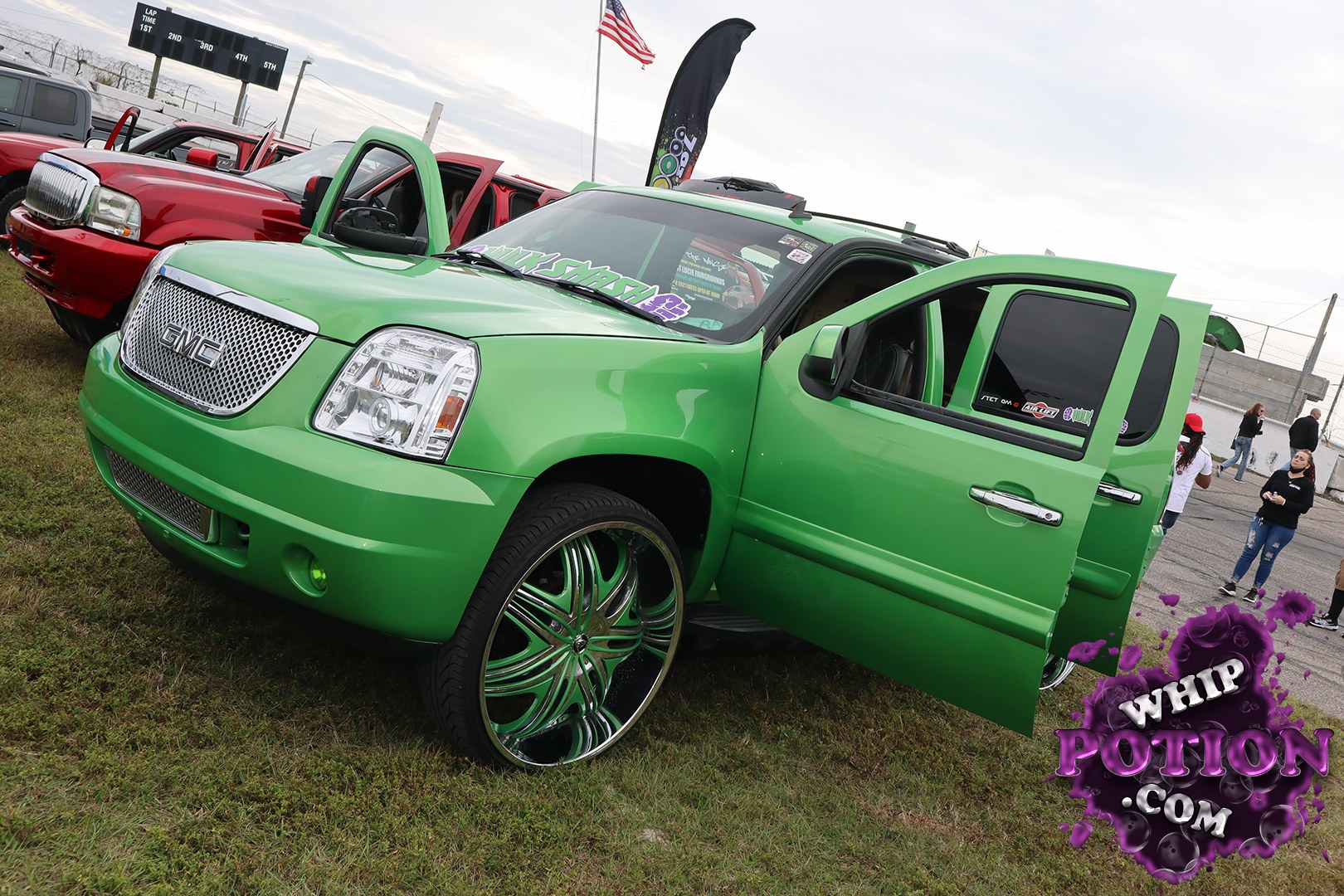 A bright green GMC SUV sits on oversized chrome-and-green custom wheels, with its doors open to show a clean, billet-style cabin and a heavily personalized look. The matching grille, smooth bodywork, and slammed stance give it that full custom show-truck vibe without losing the factory lines that make the Yukon shape so recognizable.