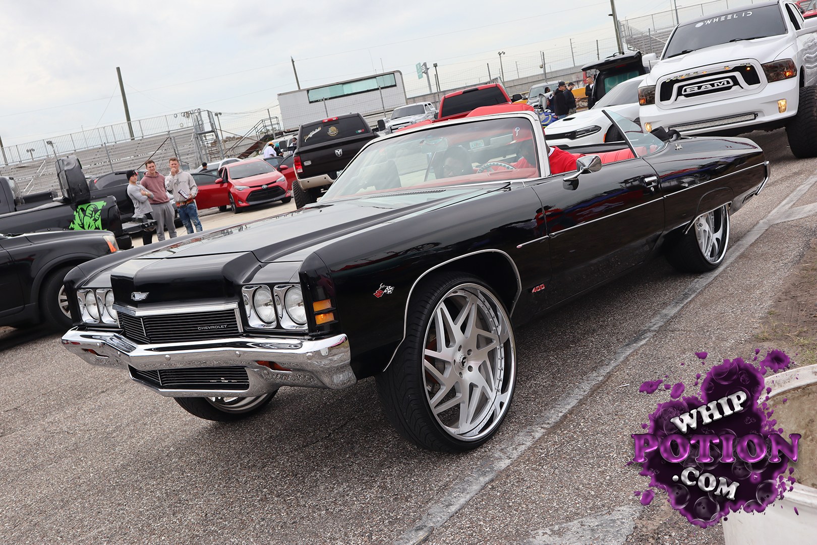 A black Chevrolet Impala convertible sits low and long with the kind of presence only a full-size drop-top can pull off. The chrome bumpers and quad headlights give it a clean vintage face, while the oversized multi-spoke wheels and red interior add a sharp custom touch that fits the car’s boulevard-cruiser attitude perfectly.
