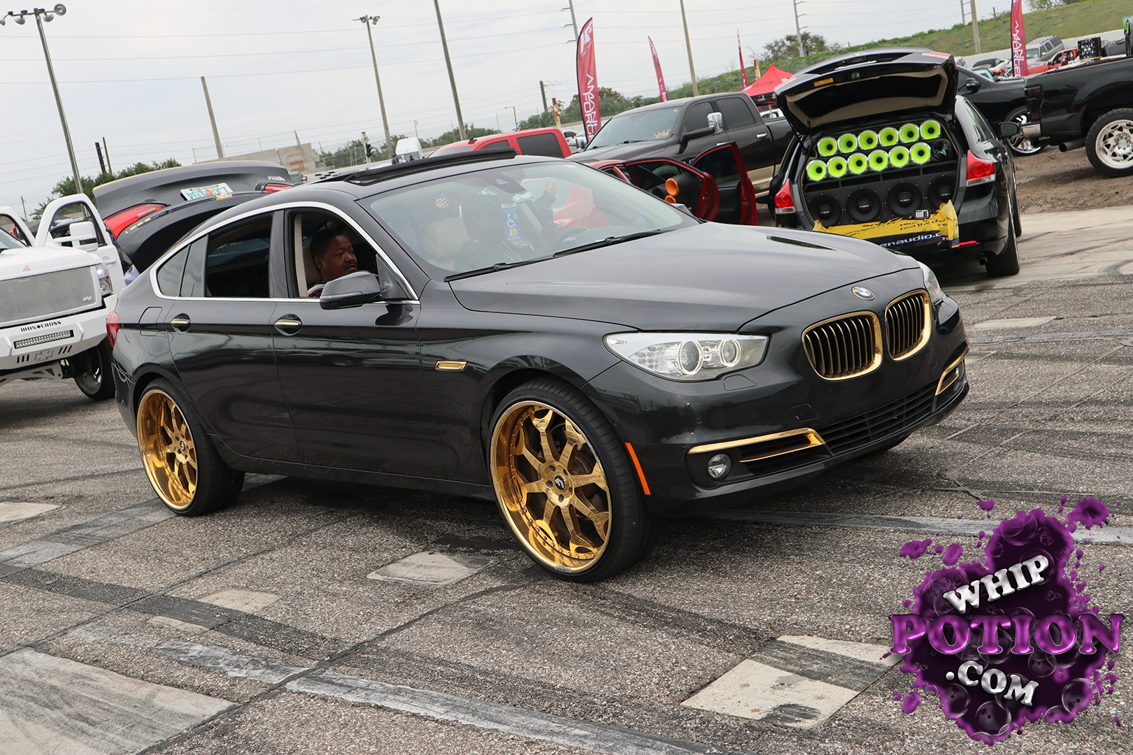 A black BMW 5 Series Gran Turismo gets a bold custom treatment with gold accents, big matching multi-spoke wheels, and a clean lowered stance that fills the arches just right. The hatch is open on a serious rear audio setup in the background, and the whole build has that polished show-car attitude without losing its street-driven feel.
