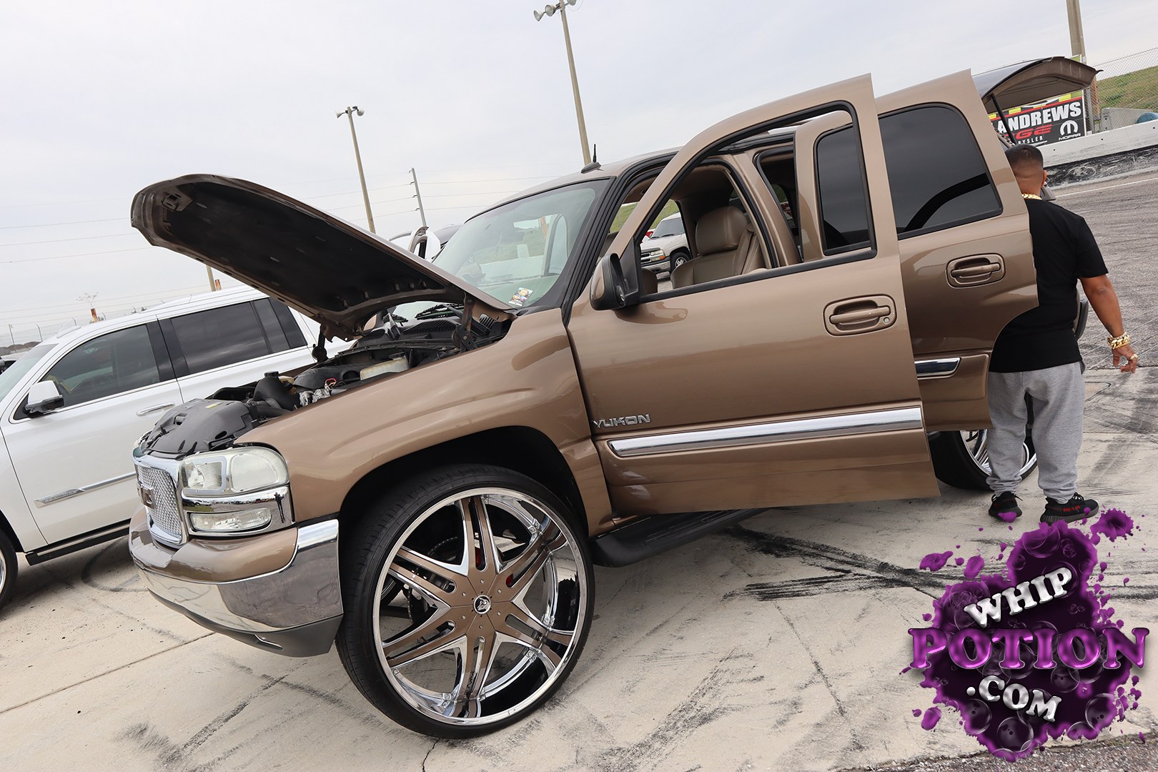 A GMC Yukon gets the full custom-truck treatment here, painted in a rich bronze two-tone with the hood up and the doors open to show off the cabin. The oversized chrome-and-bronze wheels fill the wells hard, giving it that bold show stance, while the clean chrome trim and tinted glass keep the build looking polished rather than overdone.