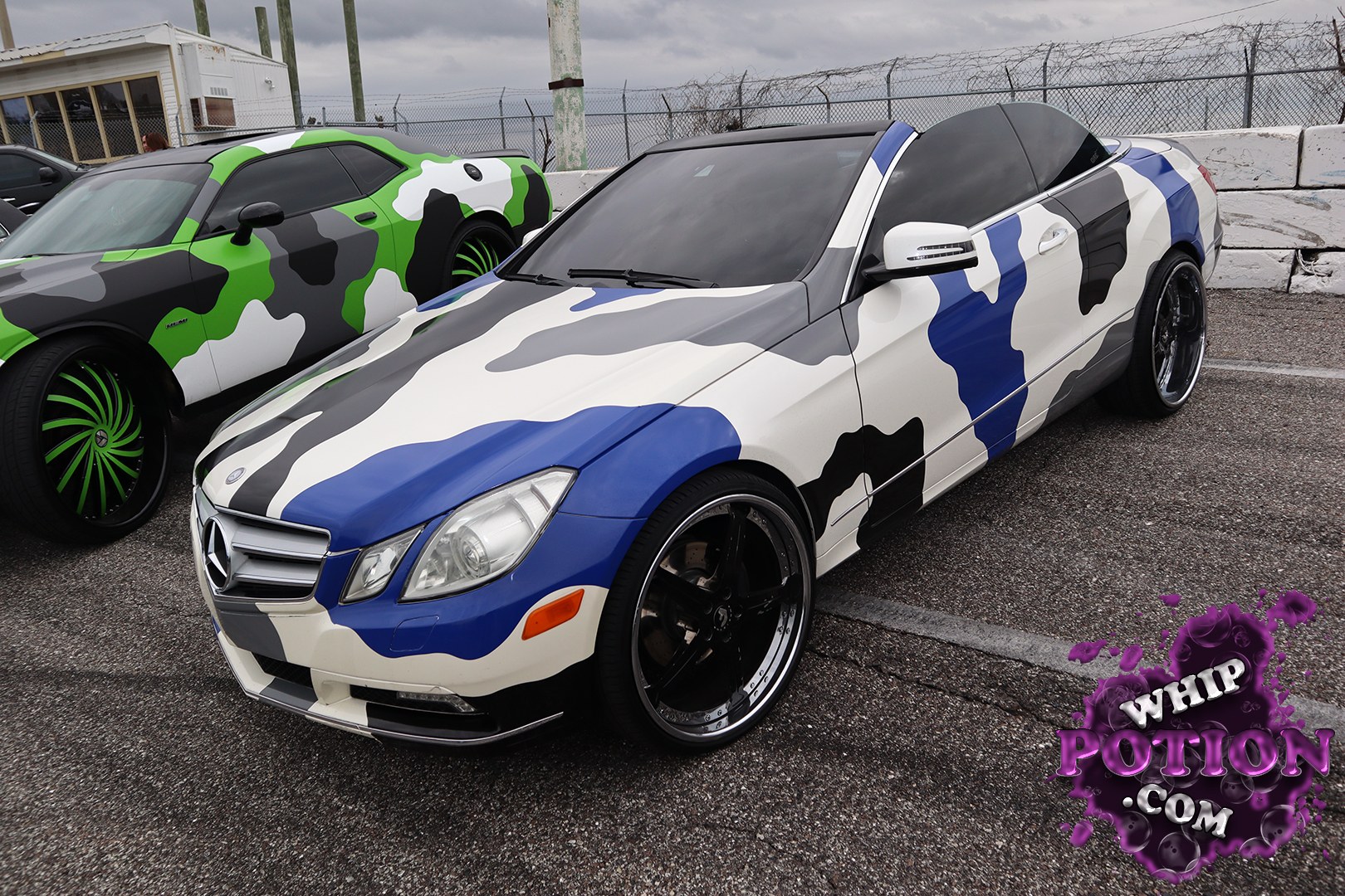 A Mercedes-Benz E-Class cabriolet gets a full custom look here, wrapped in a bold blue, white, gray, and black camo pattern that plays perfectly against the sleek body lines. The black hardtop-like roof treatment, tinted glass, and deep-dish black wheels give it a clean, aggressive stance without overdoing it.