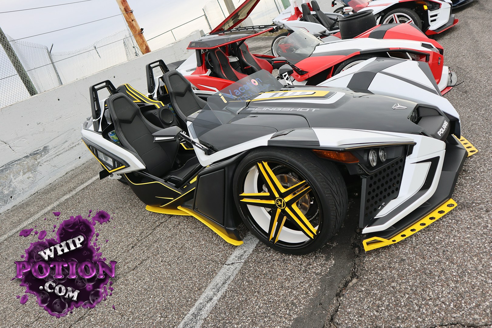 A wild Polaris Slingshot lineup sits in full custom trim, led by a black, white, and yellow machine with sharp aero pieces, matching blade-style wheels, and a low, street-scraping stance. The open cockpit and race-inspired bodywork give it more show car attitude than stock toy, with the red and white builds behind it carrying the same aggressive, personalized vibe.