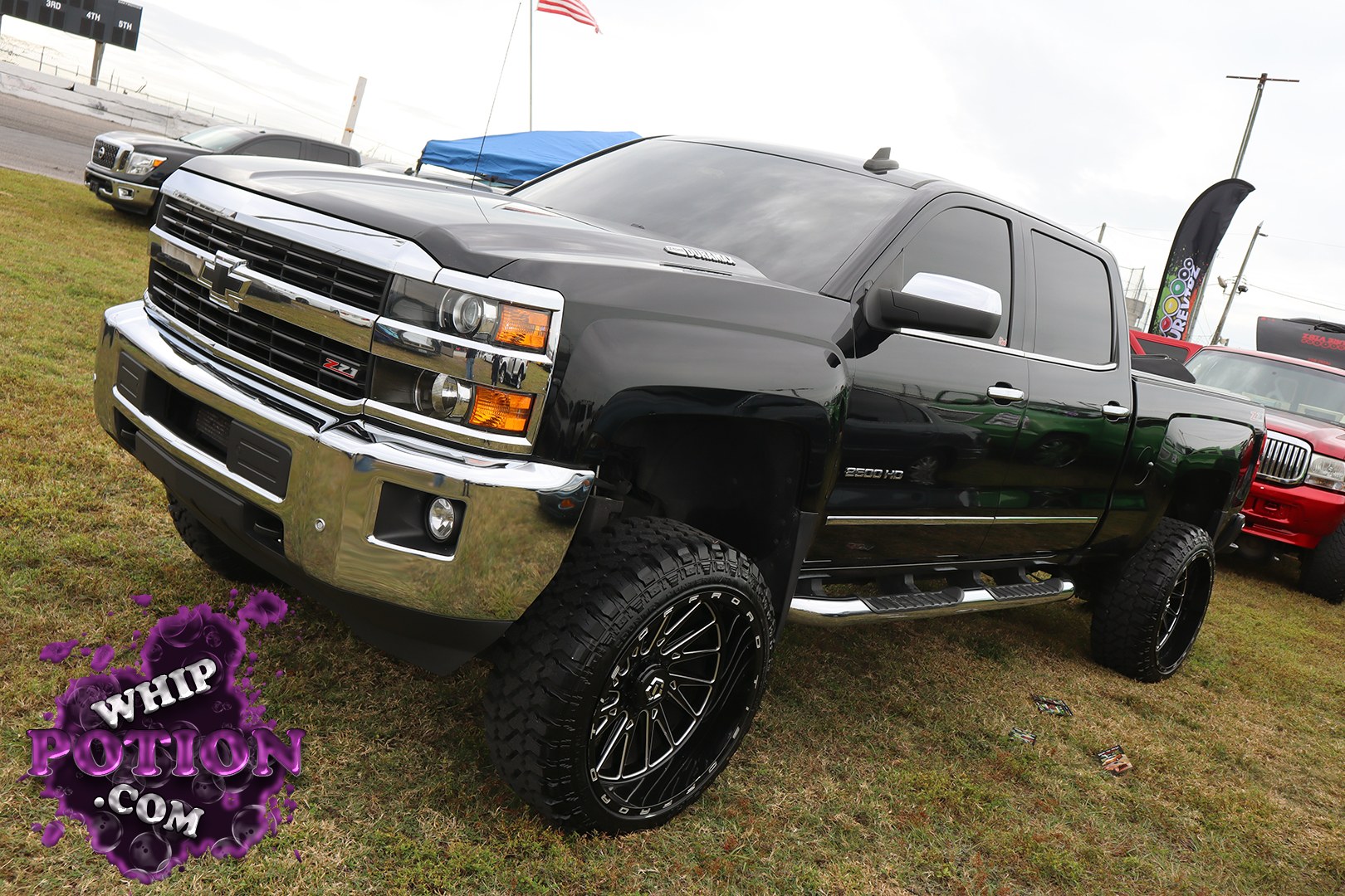 This lifted Chevrolet Silverado 2500HD wears a deep black finish, chrome-heavy front end, and a clean crew-cab profile that fits the truck show scene perfectly. Big off-road wheels and chunky tires fill the fenders, while the tinted glass, step bars, and polished grille give it a sharp, no-nonsense look at Showtime Speedway during MLK Weekend.