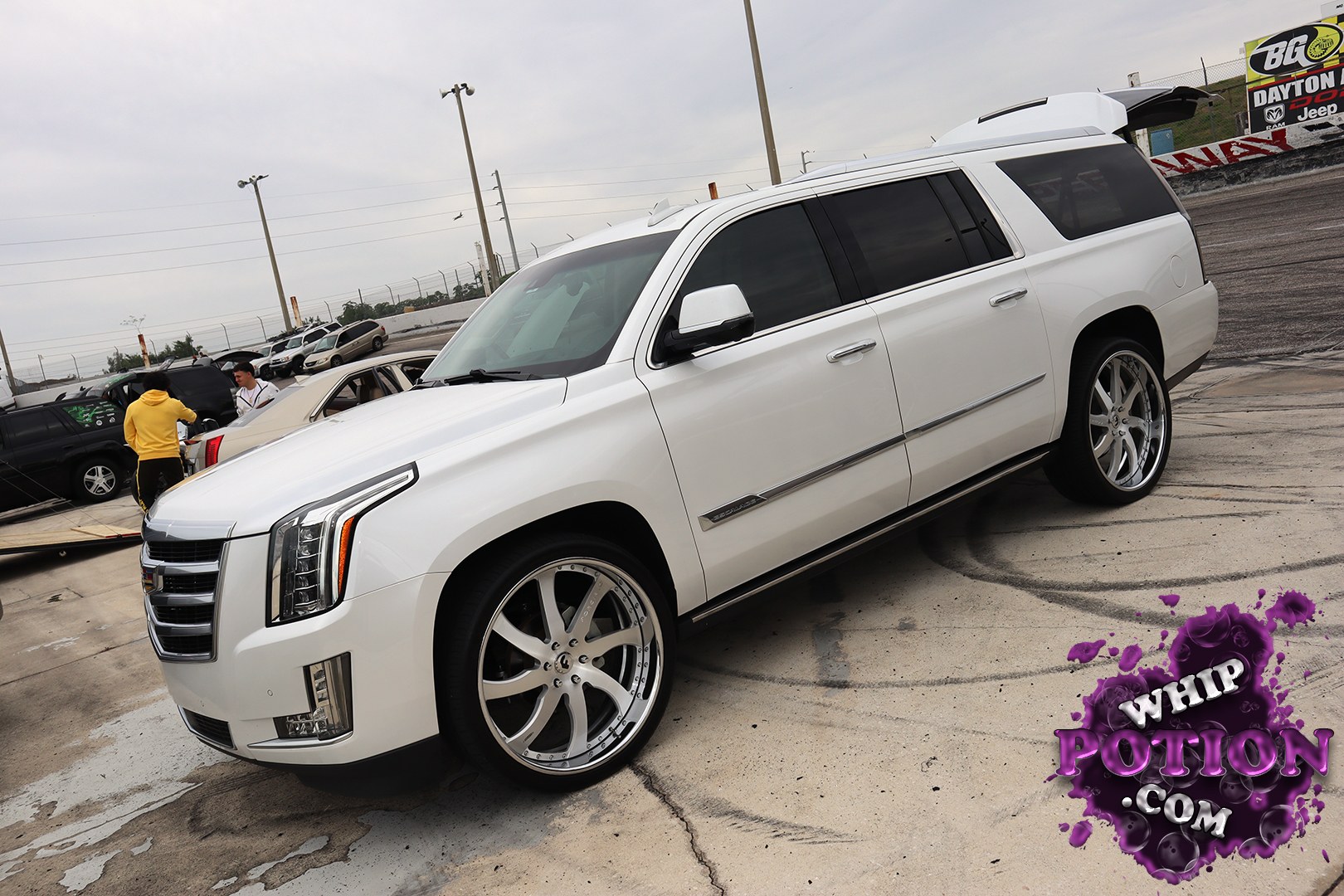 A white Cadillac Escalade sits on oversized polished multi-spoke wheels, giving this full-size luxury SUV a clean, tailored street-truck look. The deep tint, shaved-clean body sides, and factory-chrome trim keep the build classy, while the big rolling stock and low, level stance make it feel more show-ready than stock.